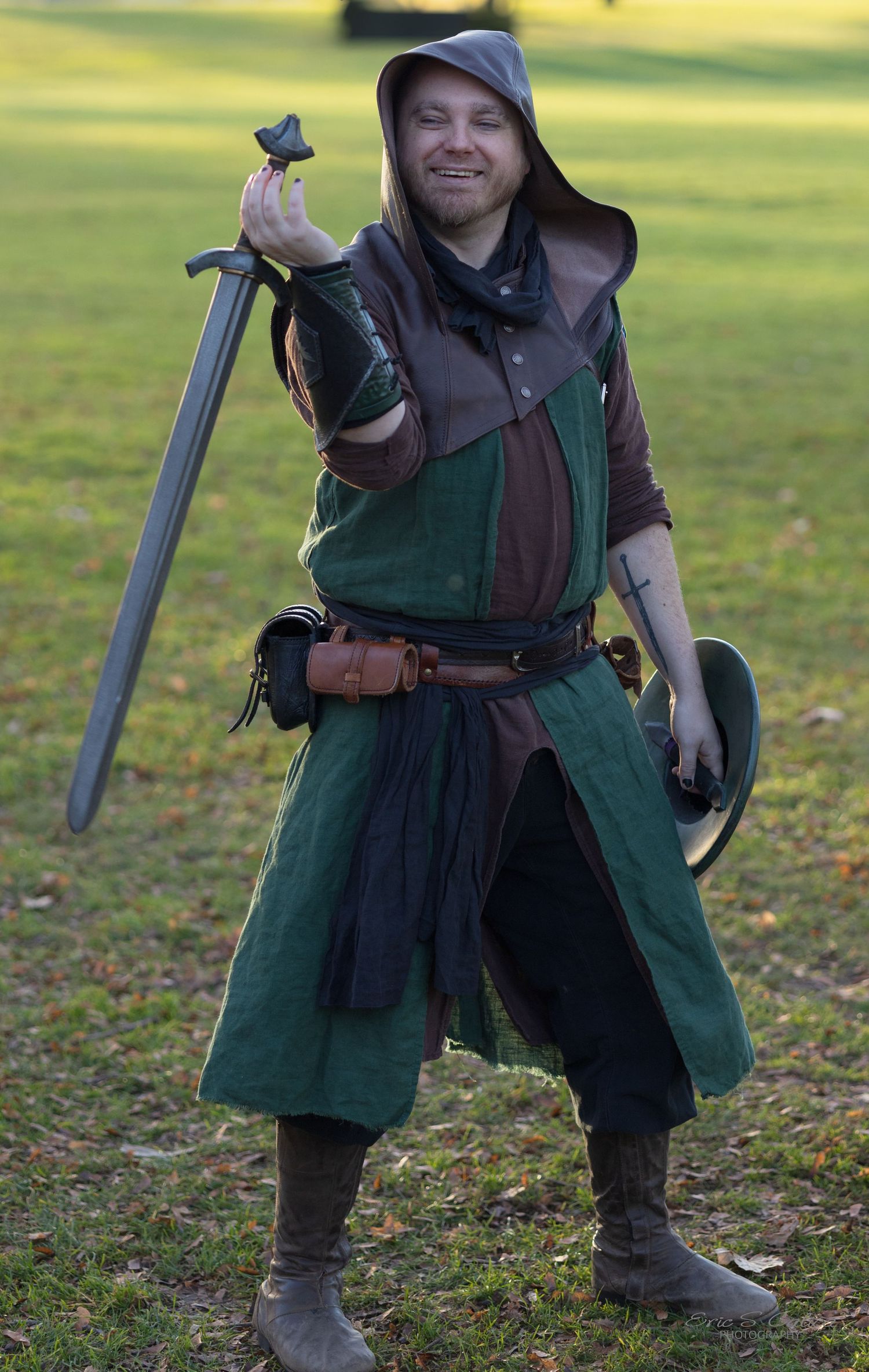 Person in medieval costume demonstrates sword moves on grassy field.
