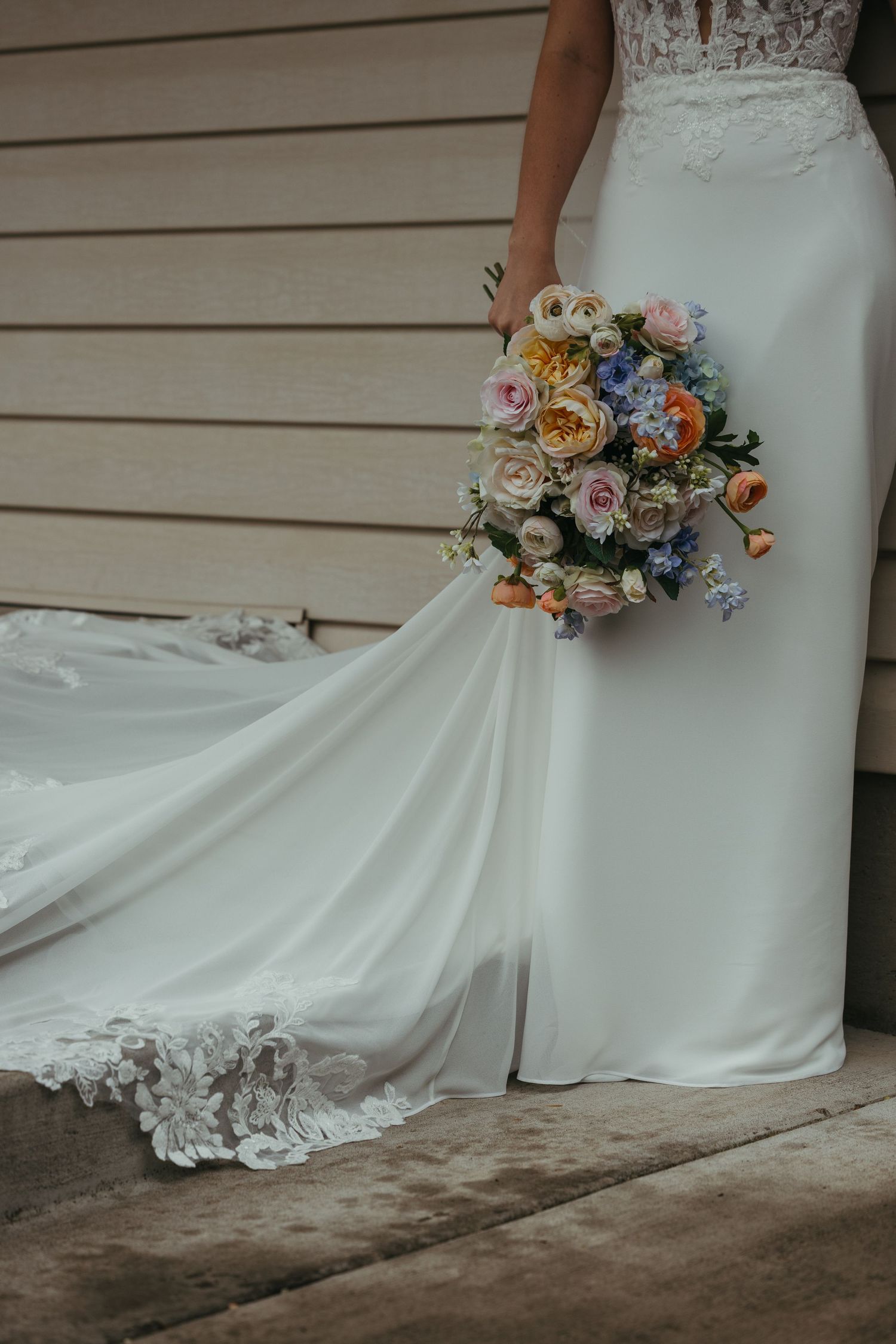 White wedding dress with lace detail and colorful floral bouquet.