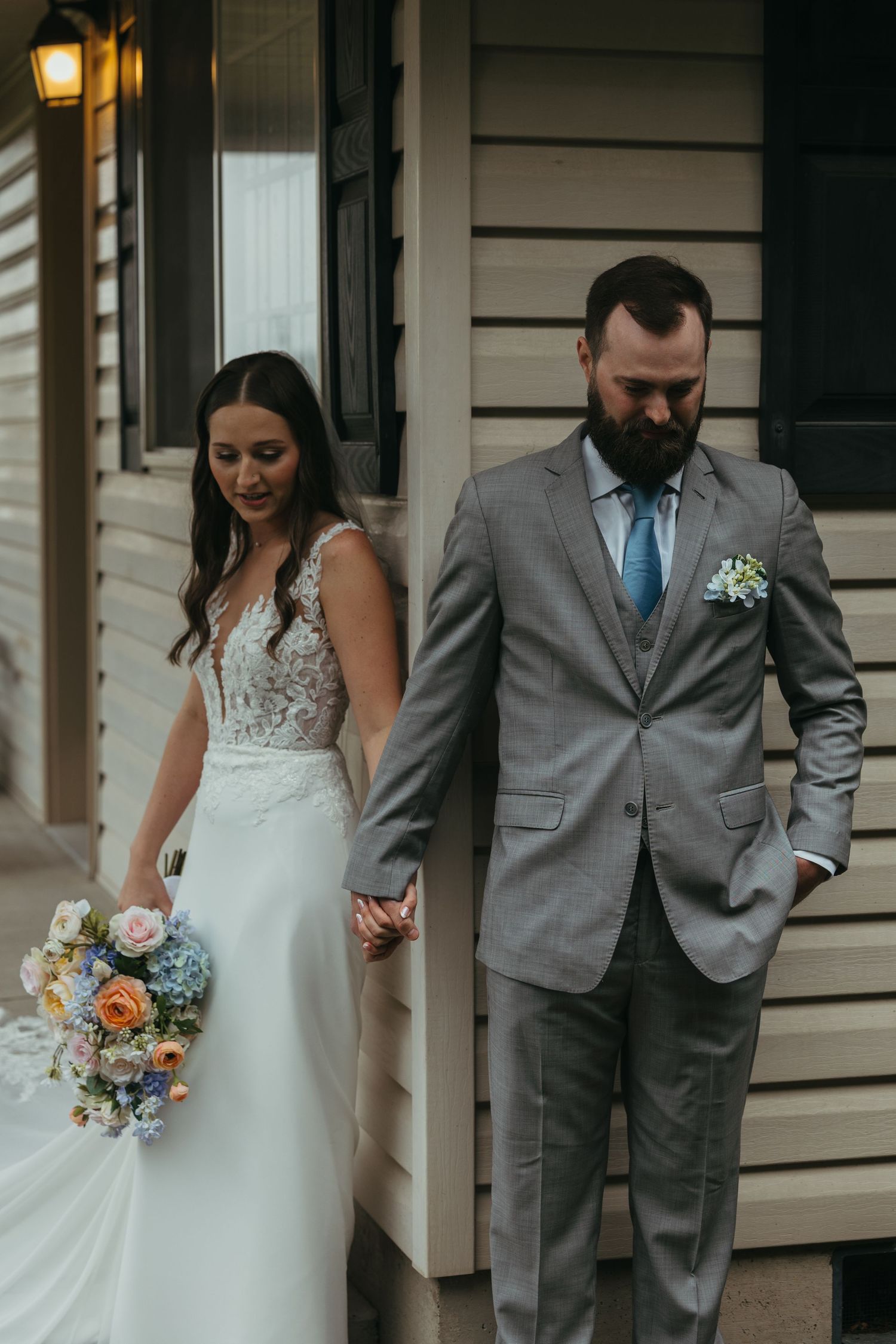 Bride and groom in wedding attire posing by a rustic porch with white siding.