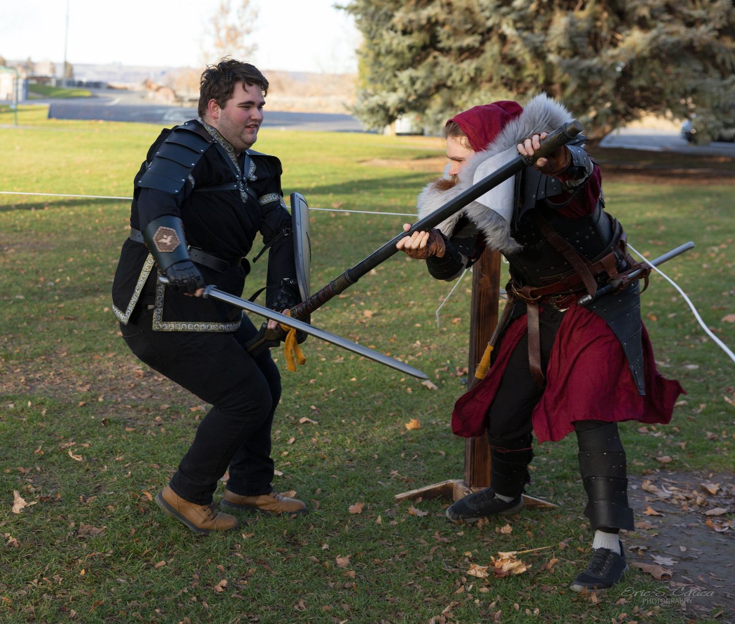 People in medieval costumes engage in sword combat roleplay on a grassy field.