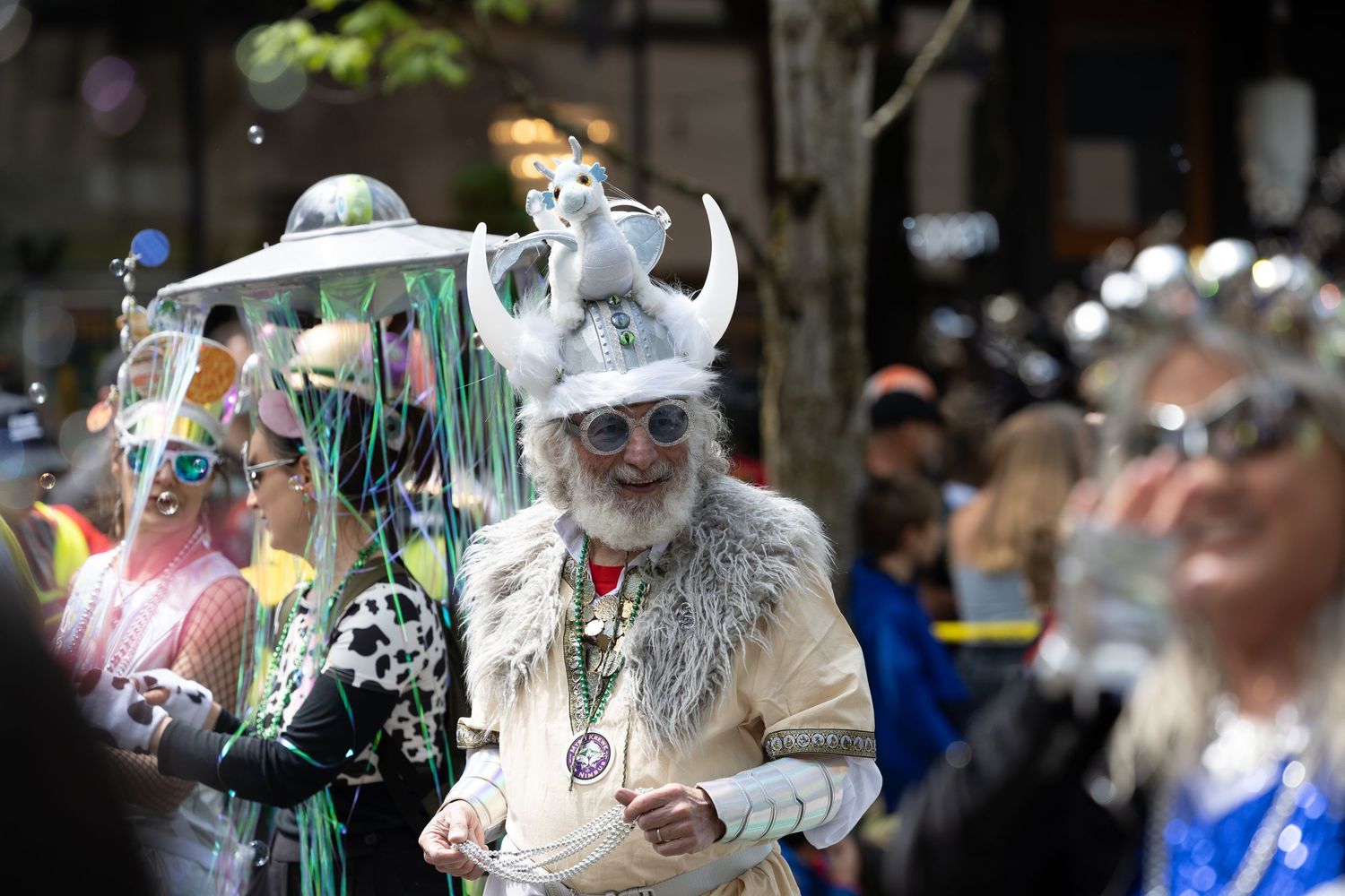 Colorful festival attendees in elaborate costumes gather on a city street during a public celebration.