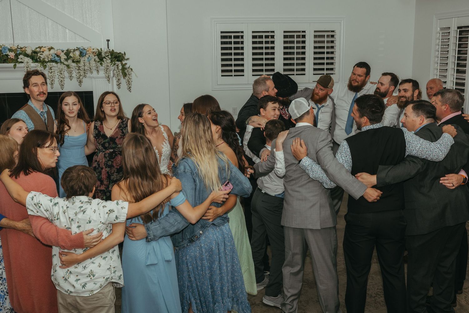 A group of wedding guests dancing and celebrating together in a white-walled room.