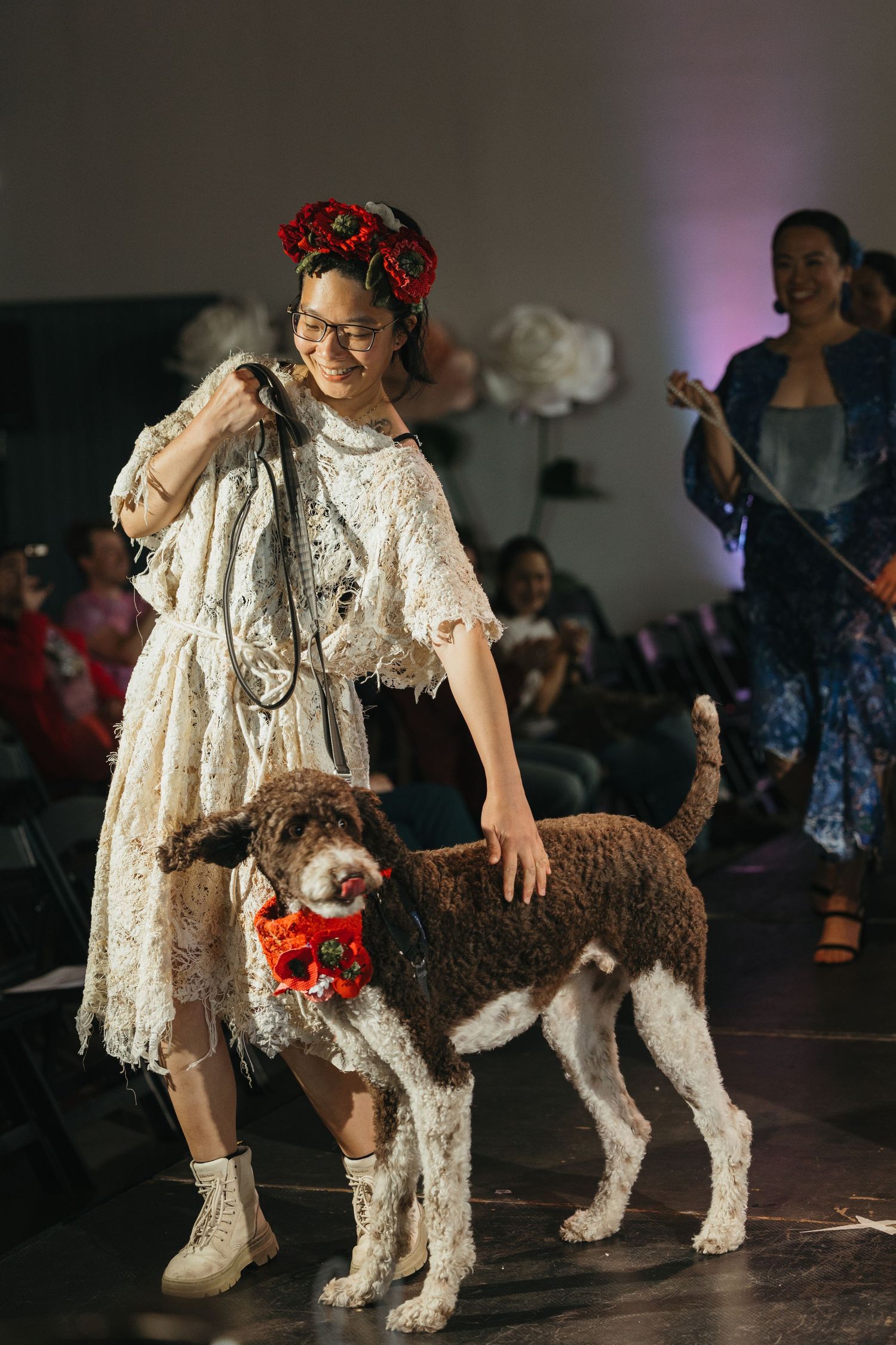A white costumed person poses with a scruffy grey and white dog on stage during a performance.