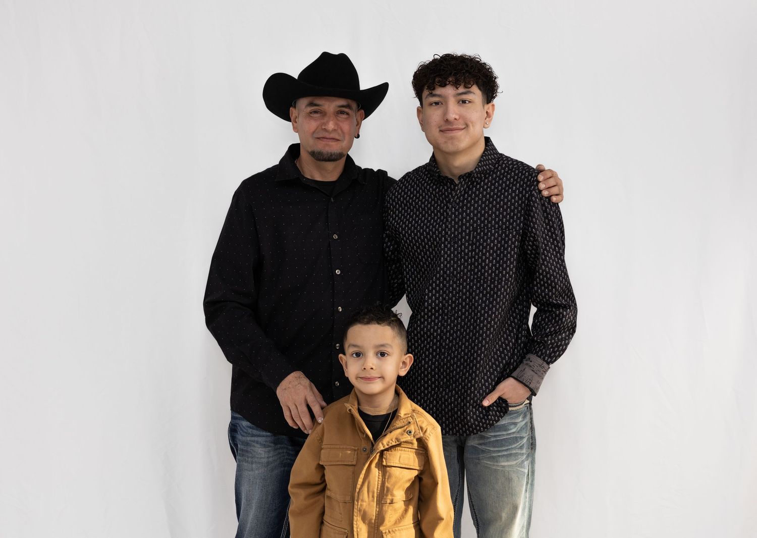 Three people pose together against a white backdrop, one wearing a cowboy hat and another in a yellow jacket.