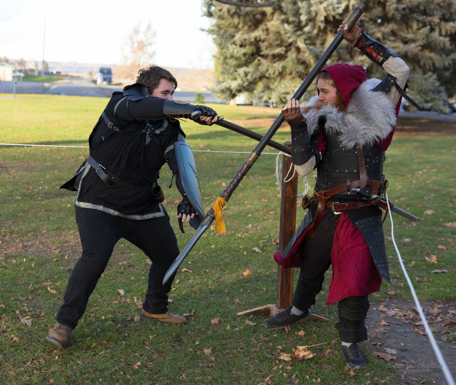 Medieval costumed performers practicing sword fighting techniques outdoors.