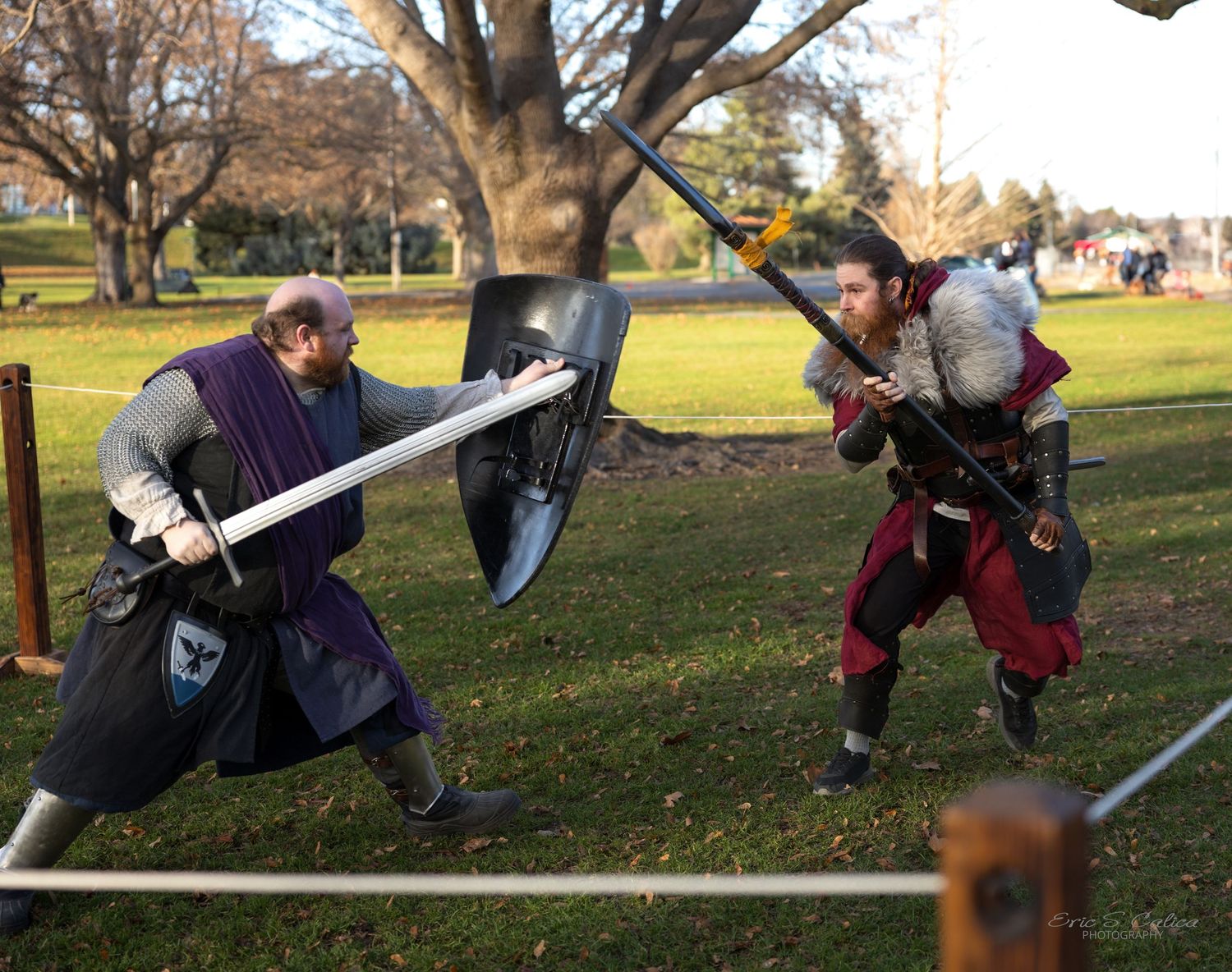 People engaged in medieval combat roleplay with foam weapons in a park setting.
