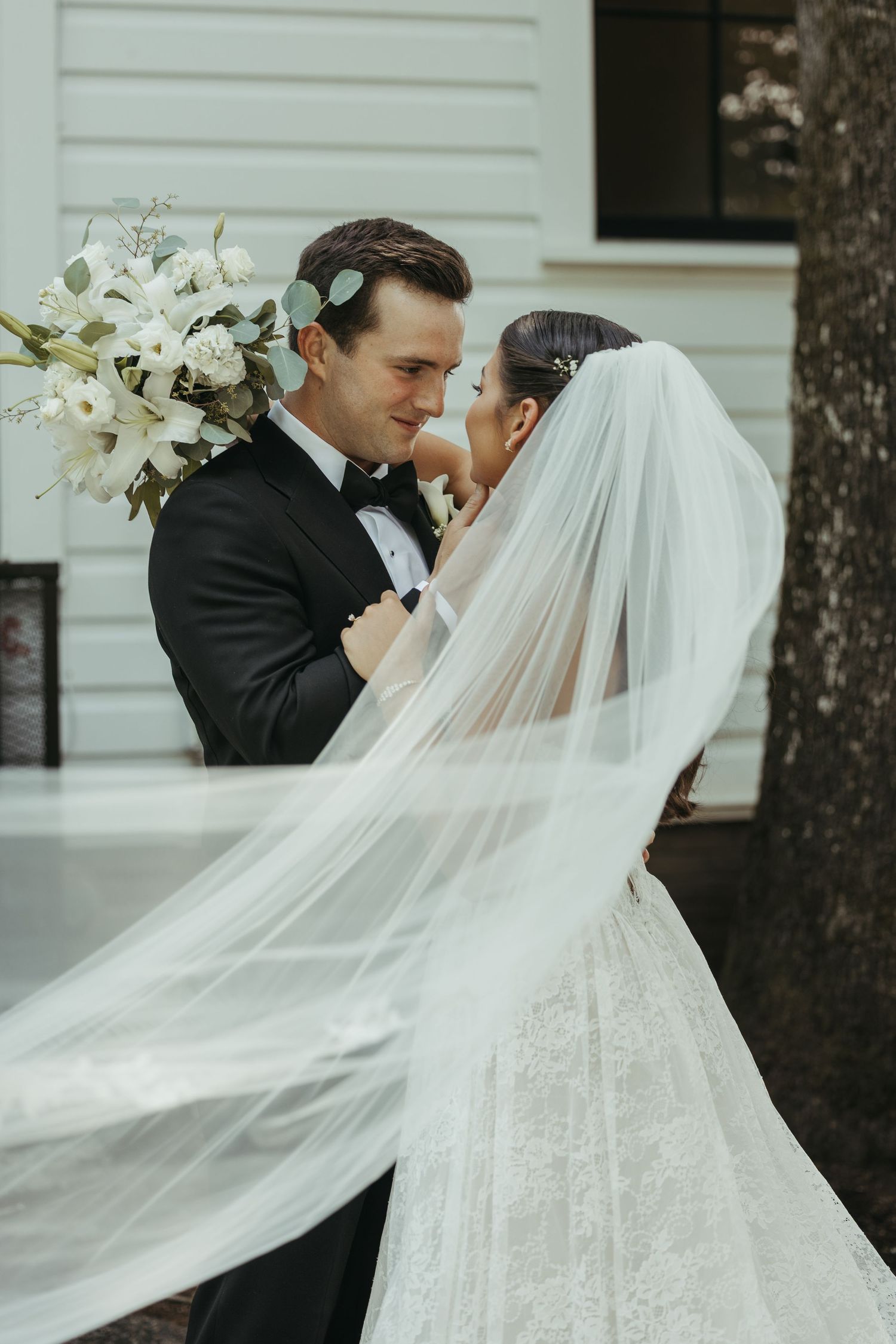 Romantic wedding portraits with a flowing cathedral veil against a white building backdrop.