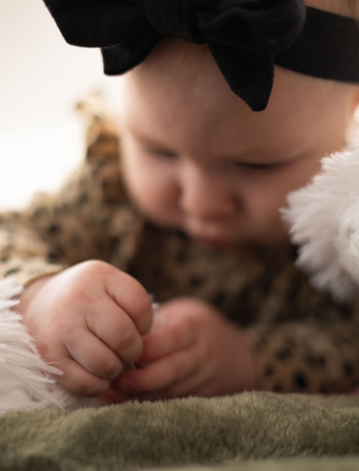 A close-up macro photo shows a baby's tiny fingers gently resting on a soft green textured surface.