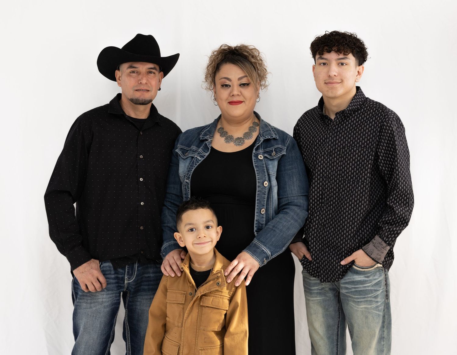 Family wearing denim and dark clothing poses together against white backdrop.