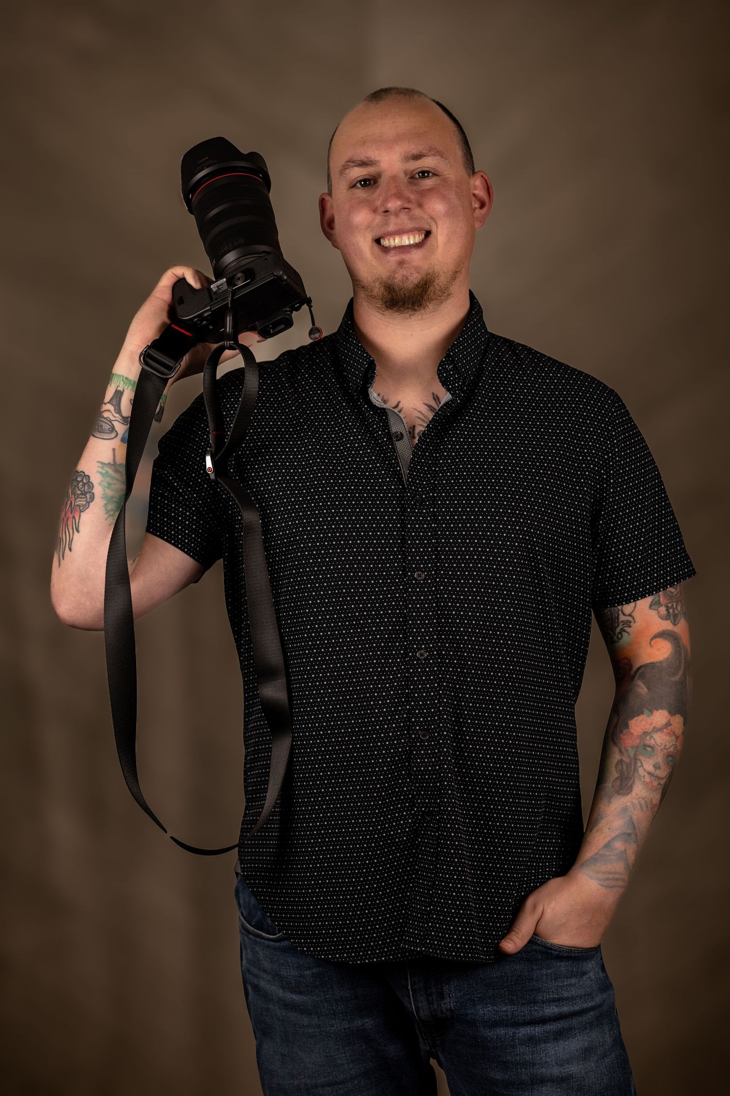 Professional photographer holding DSLR camera wearing black polka dot shirt.