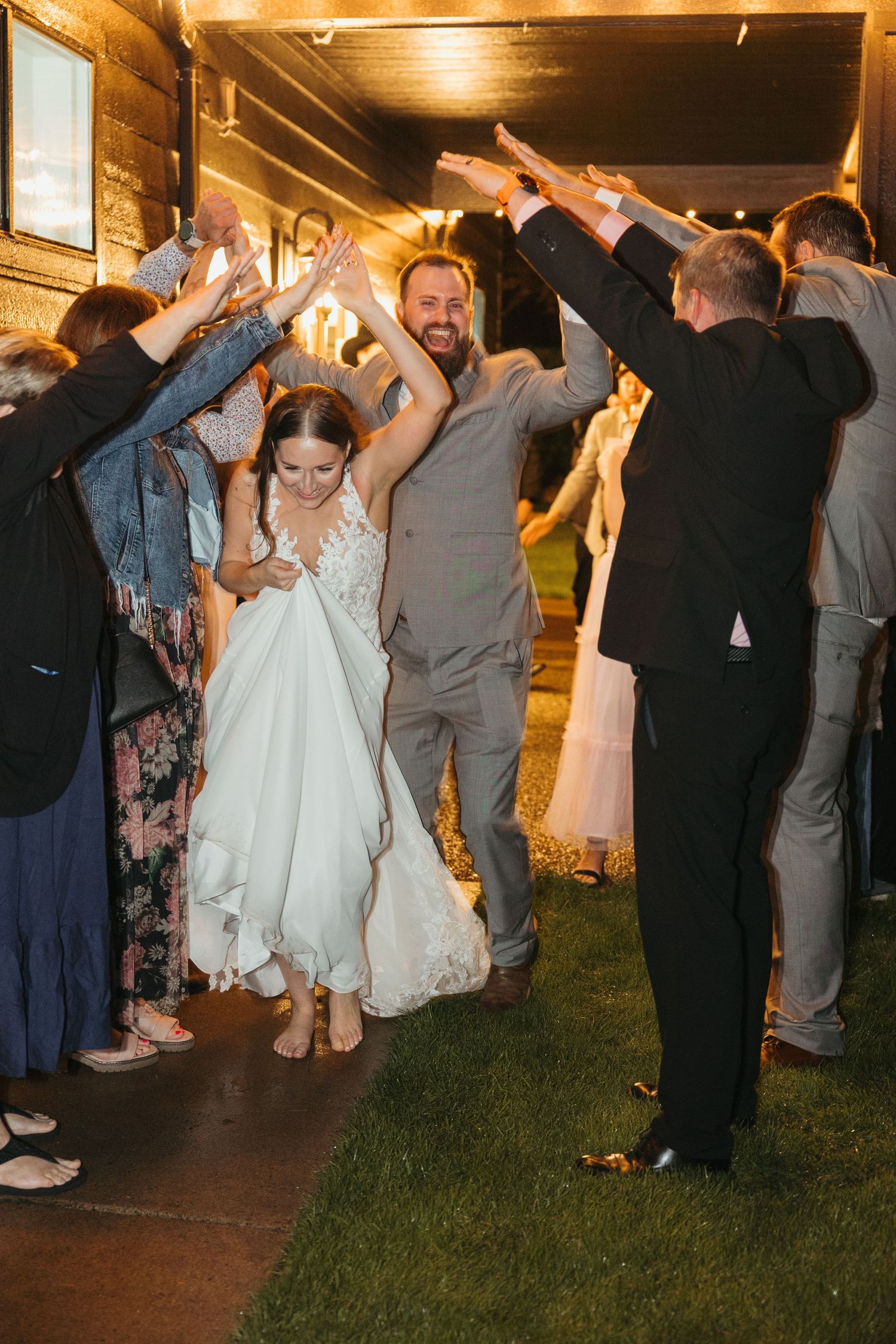 Wedding guests form a tunnel with raised arms as newlyweds walk through.