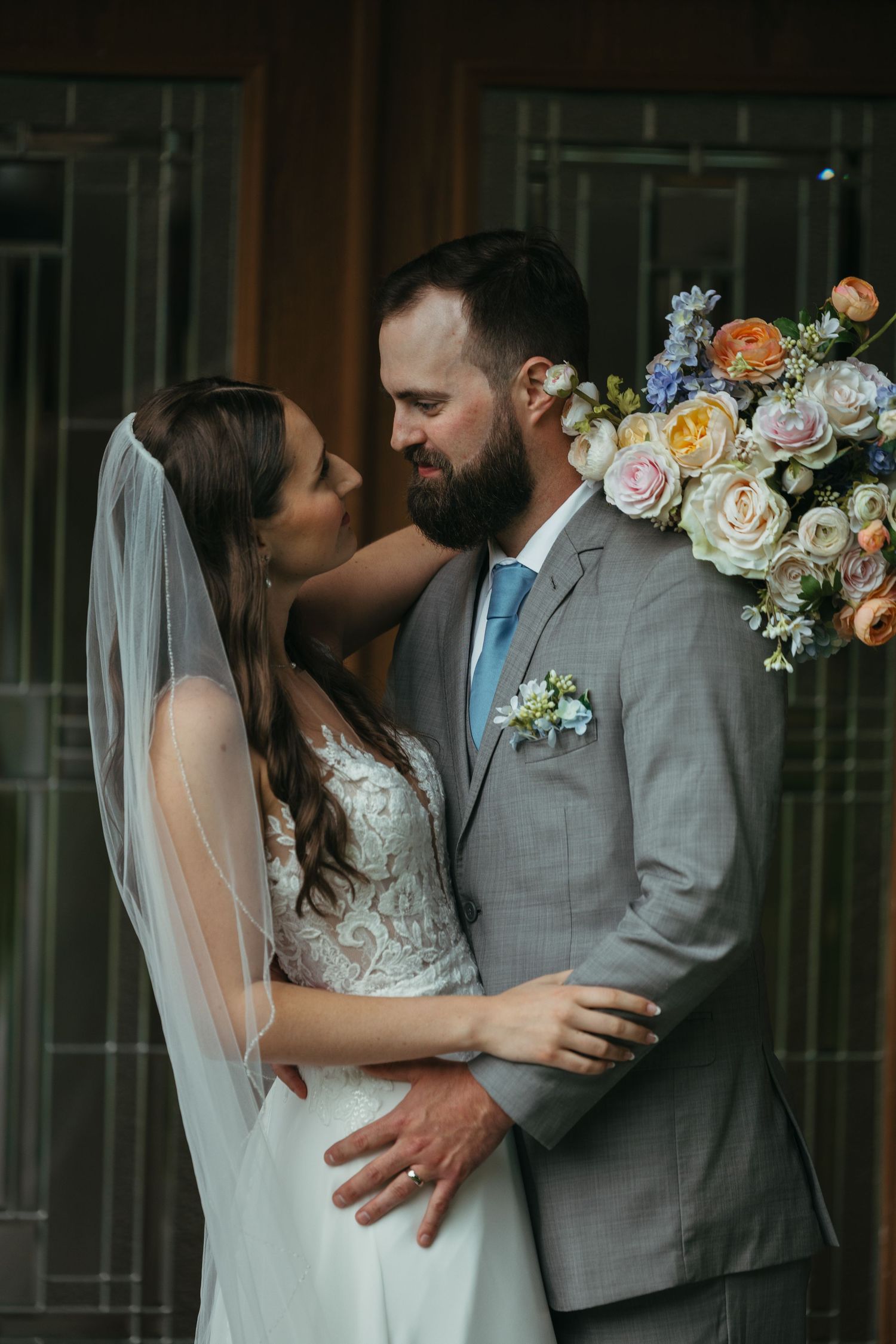 Romantic wedding couple poses with floral arrangements in an intimate indoor setting.
