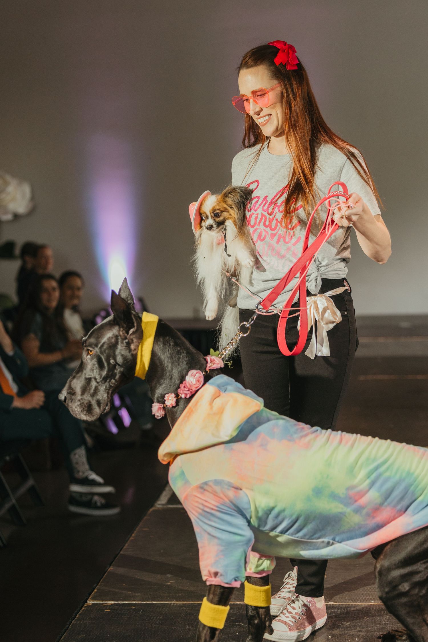 Performer in tie-dye outfit with red accessories dances on a dark stage.