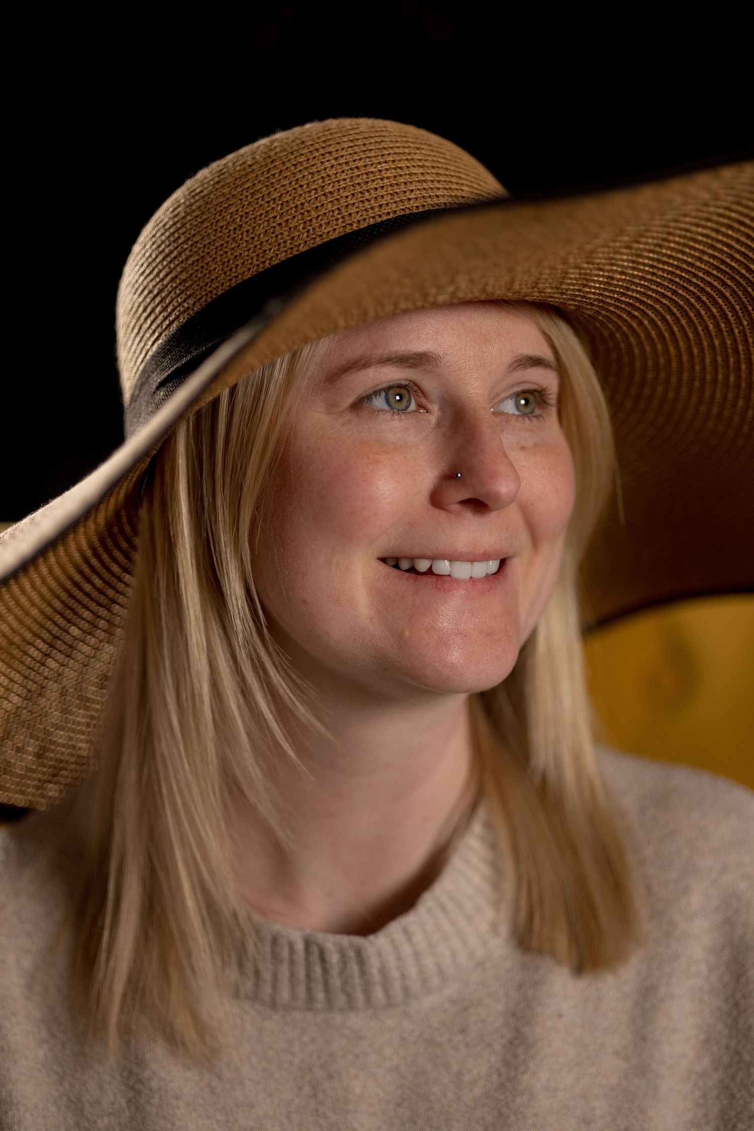 Portrait of someone wearing a wide-brimmed straw sunhat and beige sweater with soft lighting.