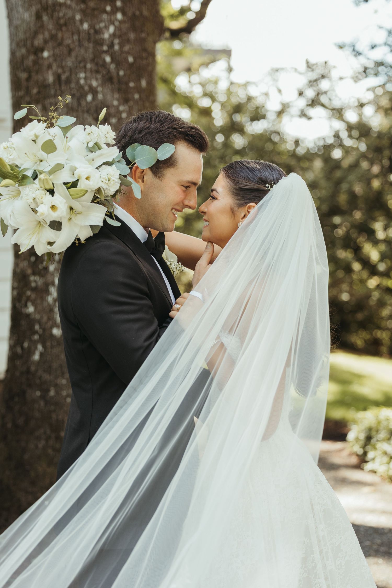 Romantic wedding portrait captured outdoors with flowing veil and white floral decorations.