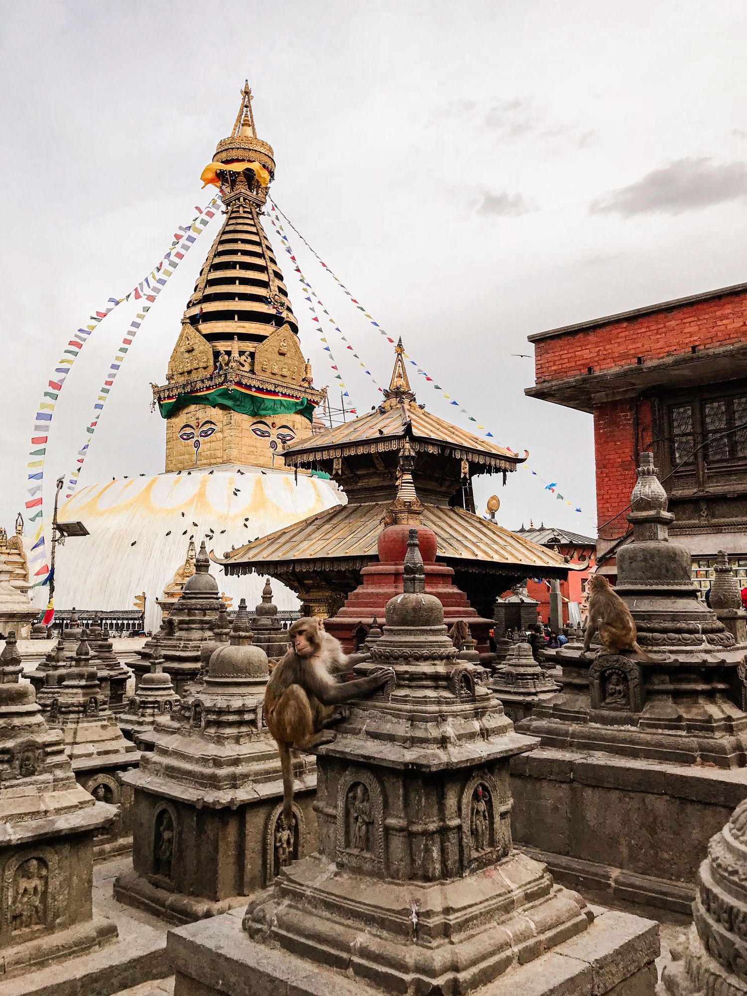 Ancient Buddhist temple complex with multiple stupas and prayer flags against cloudy sky.