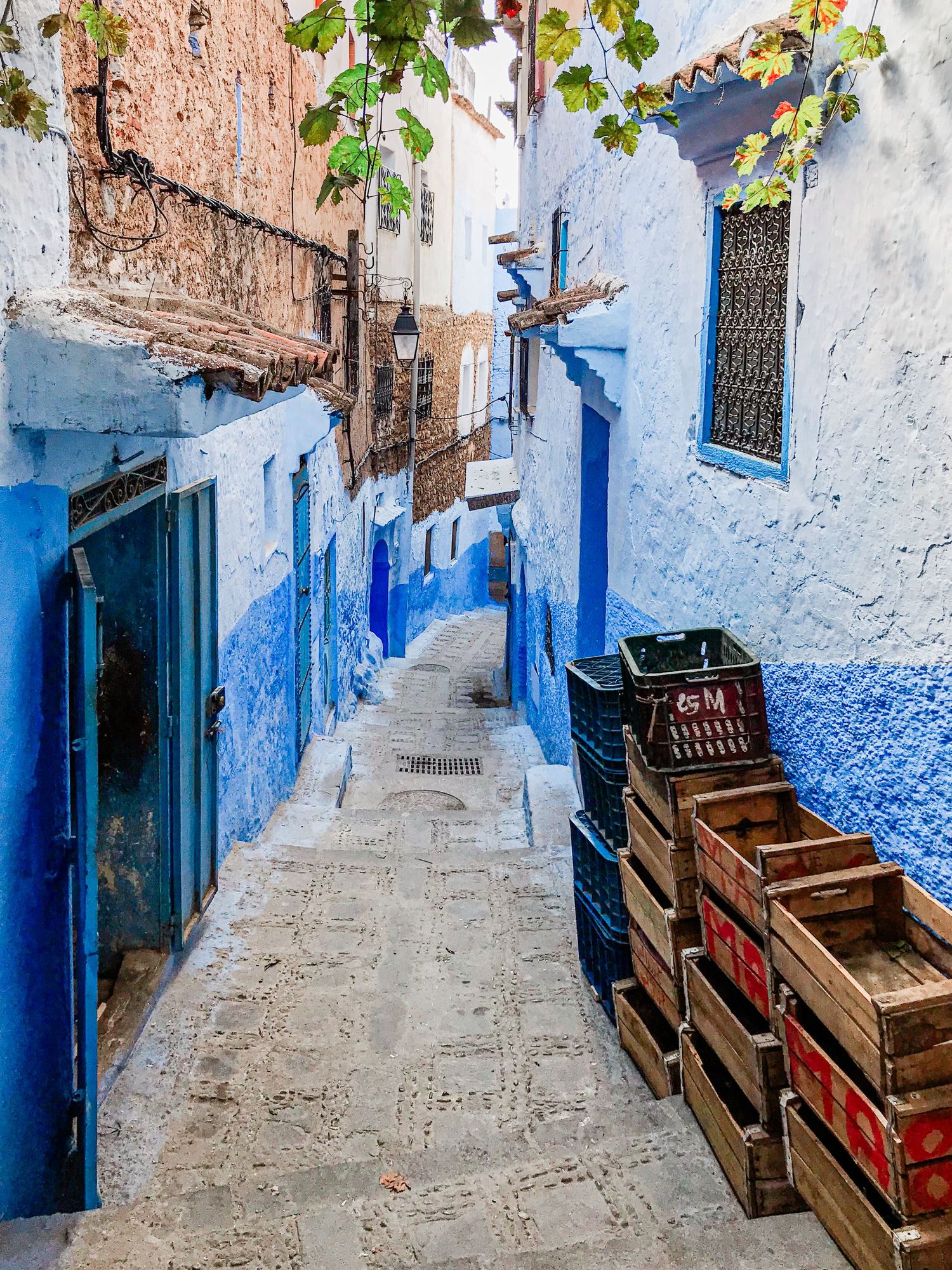 Narrow cobblestone alley with blue-washed walls and wooden crates in a Moroccan medina.