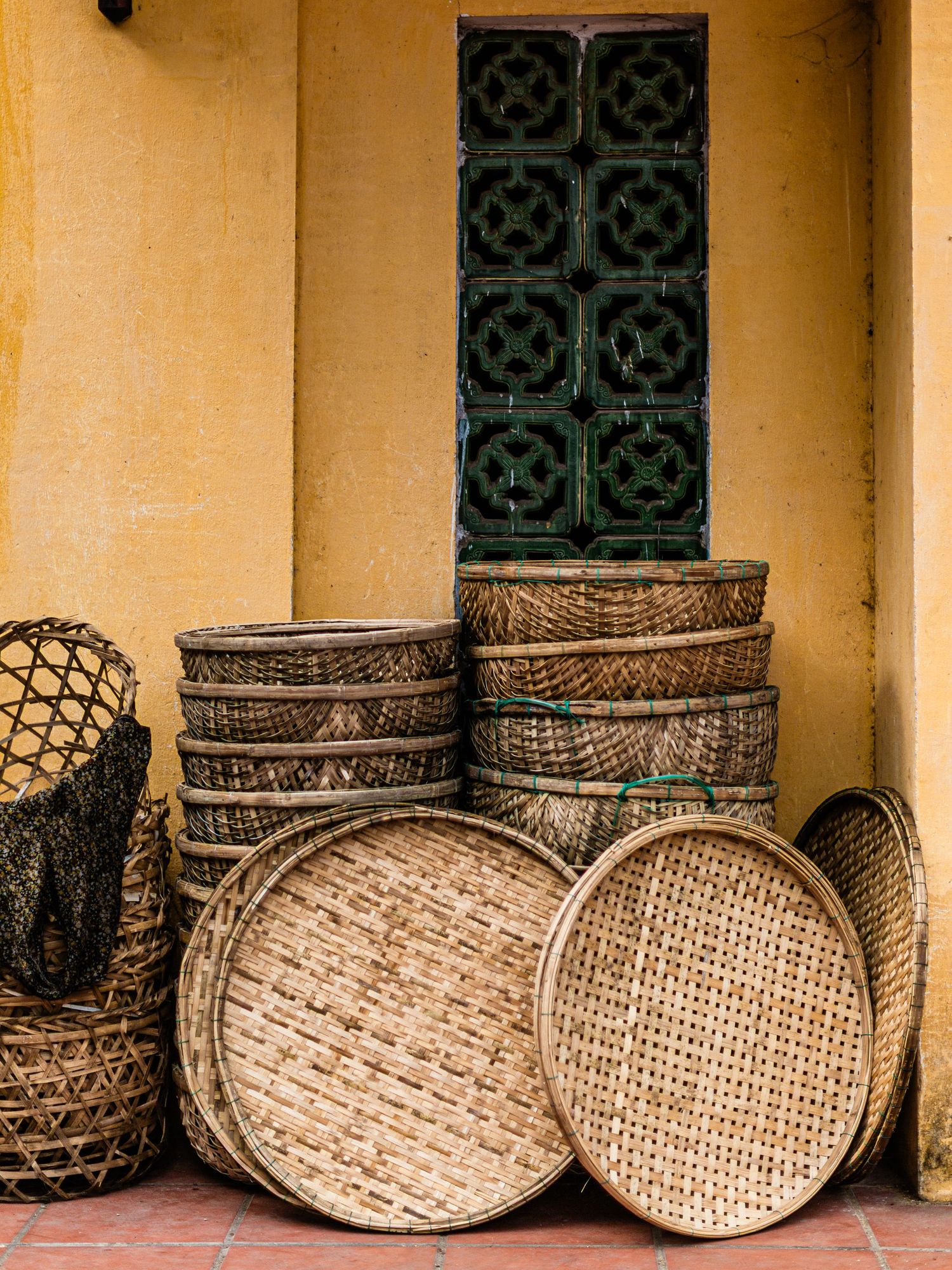 Stack of traditional woven bamboo baskets against a yellow wall with decorative window.