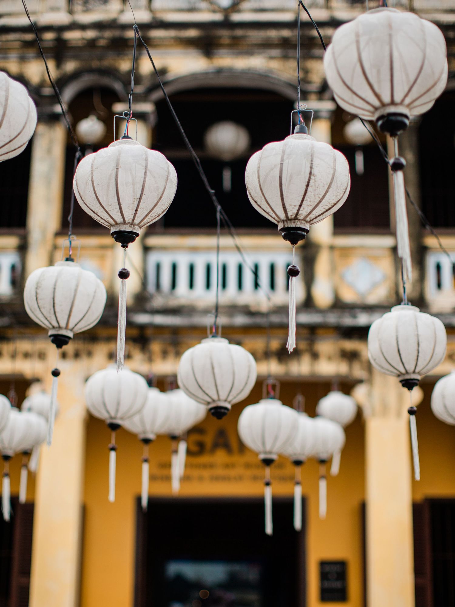 Row of white paper lanterns hanging from a ceiling against a yellow wall.