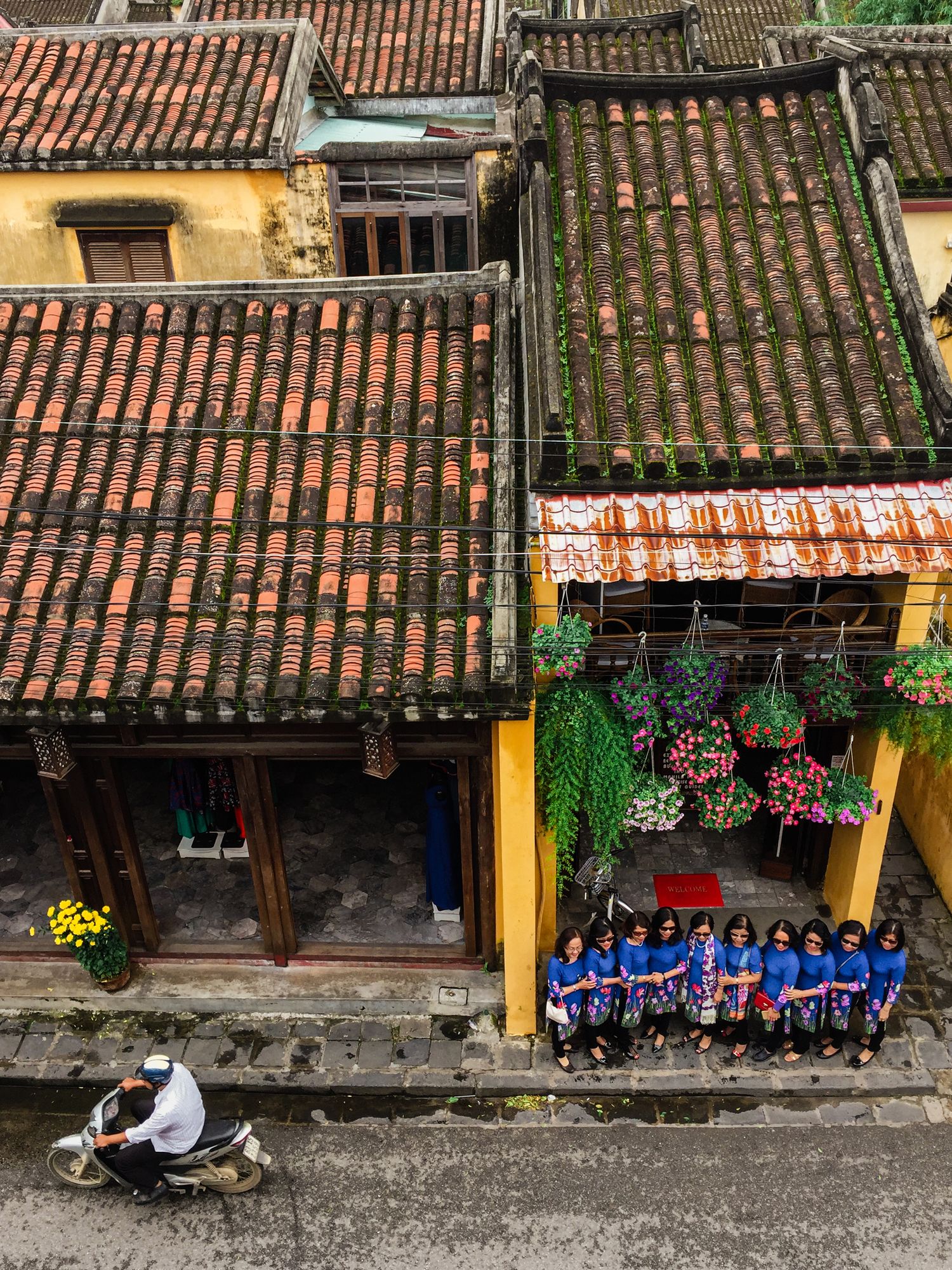 Group seated outside traditional building with yellow walls and terracotta tiled roof in Asian architectural style.