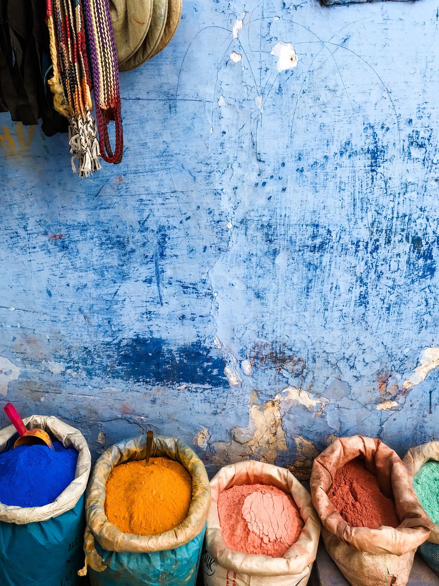 Colorful spices in burlap sacks displayed against a weathered blue wall in Morocco.
