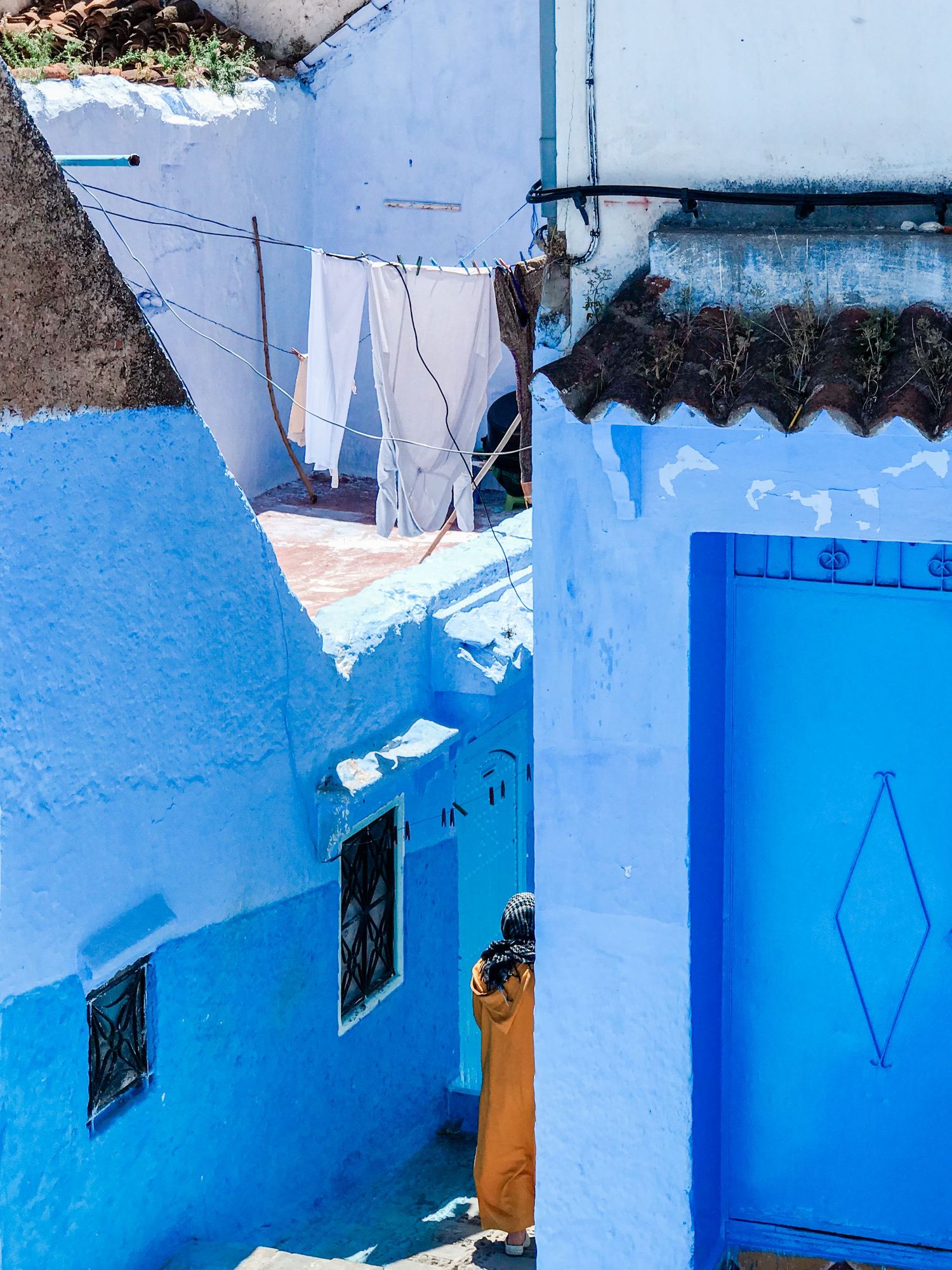 Series of blue painted doorways and geometric patterns along a narrow Moroccan street.