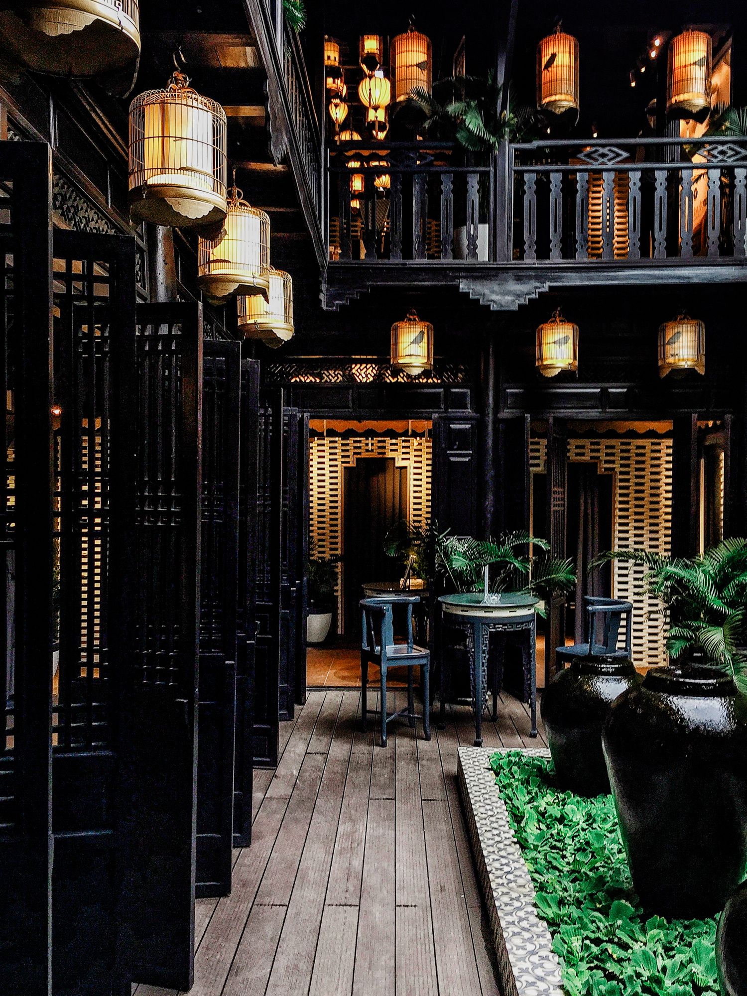 Dark wooden corridor with glowing lanterns and potted plants creating an atmospheric Asian ambiance.