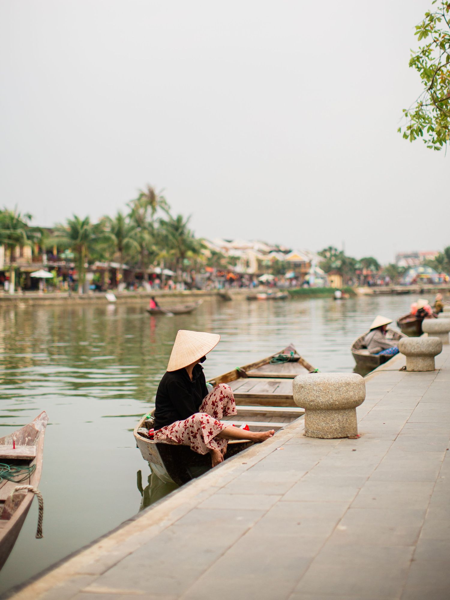 Traditional boat on Thu Bon River with waterfront buildings in Hoi An, Vietnam.