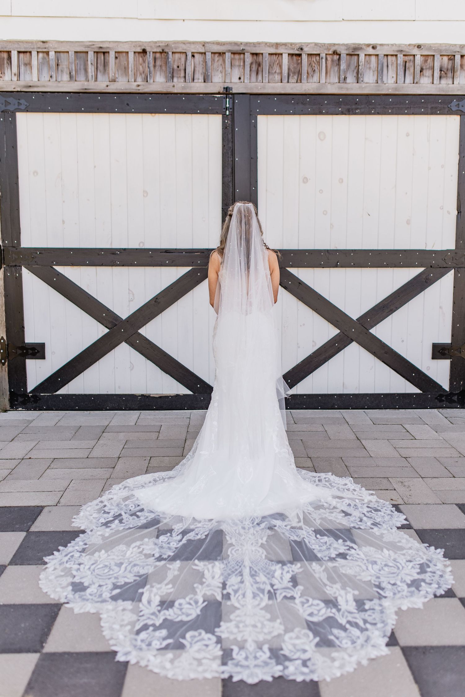 A stunning lace wedding veil with intricate floral details trails behind  rustic barn doors, local mid michigan wedding photographer