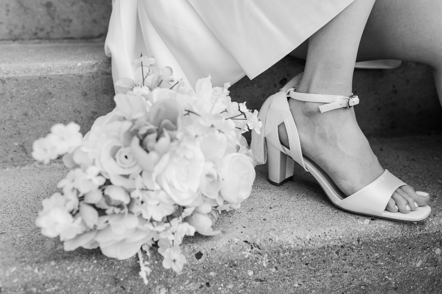 Close-up detail shots of white wedding shoes and dress hem against stone or concrete surfaces.
