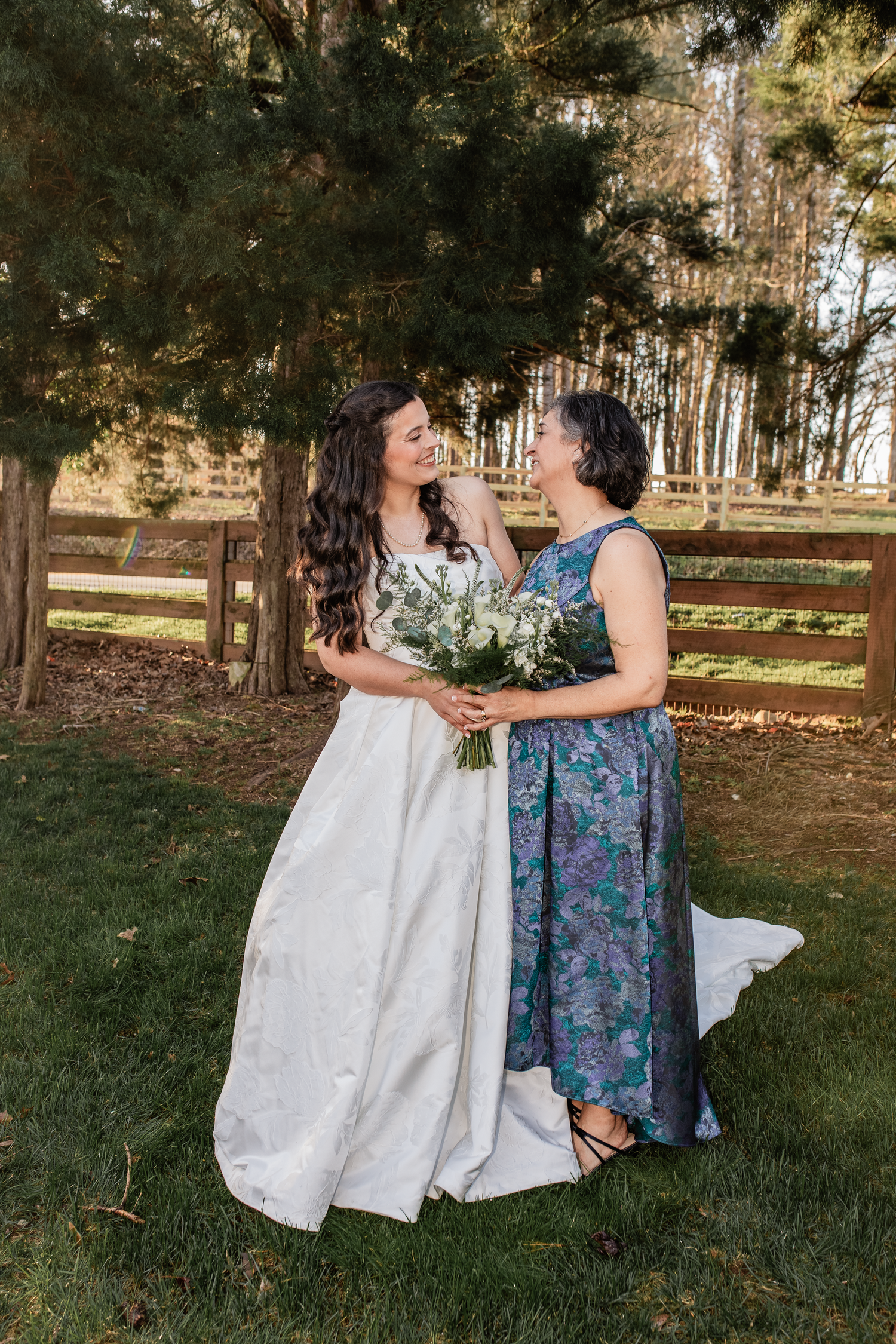 A bride in a white gown holds a bouquet while smiling with an mother of bride, Mid michigan wedding photographer