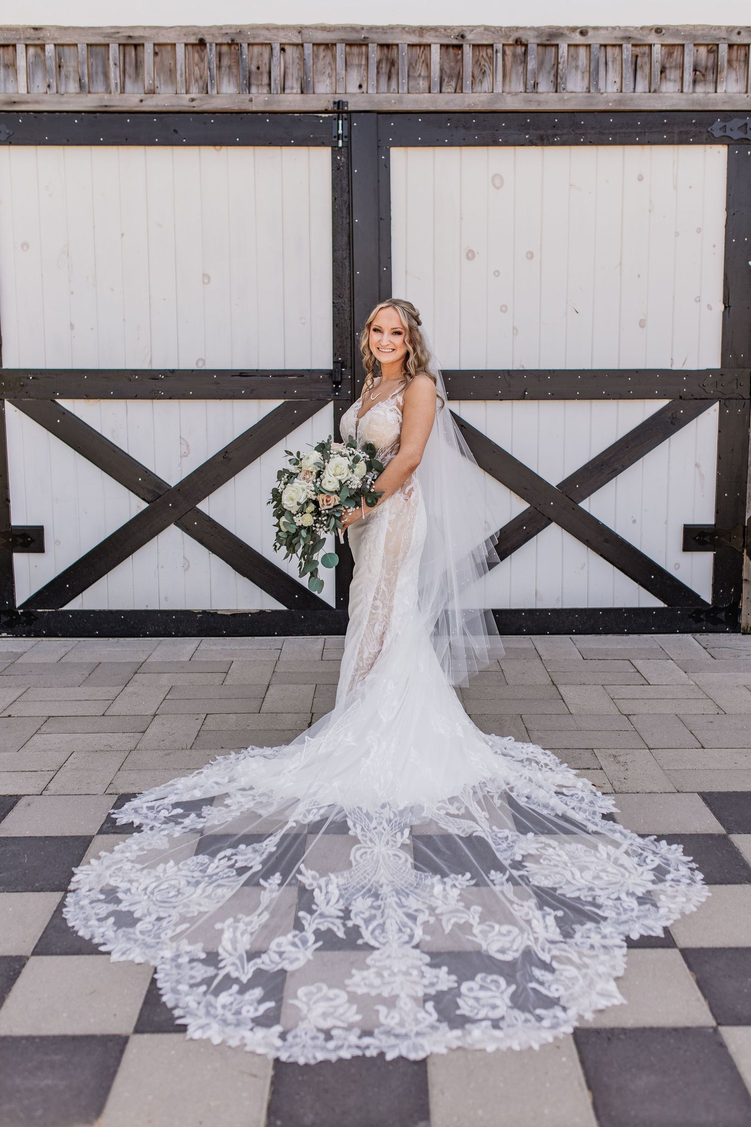 A stunning cathedral-length lace wedding veil spreads across a stone patio in a dramatic sweeping pattern.