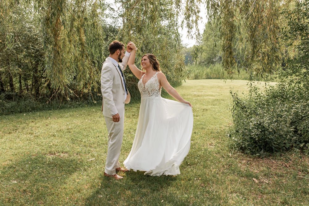 A bride and groom dance together outdoors near a weeping willow tree on their wedding day.
