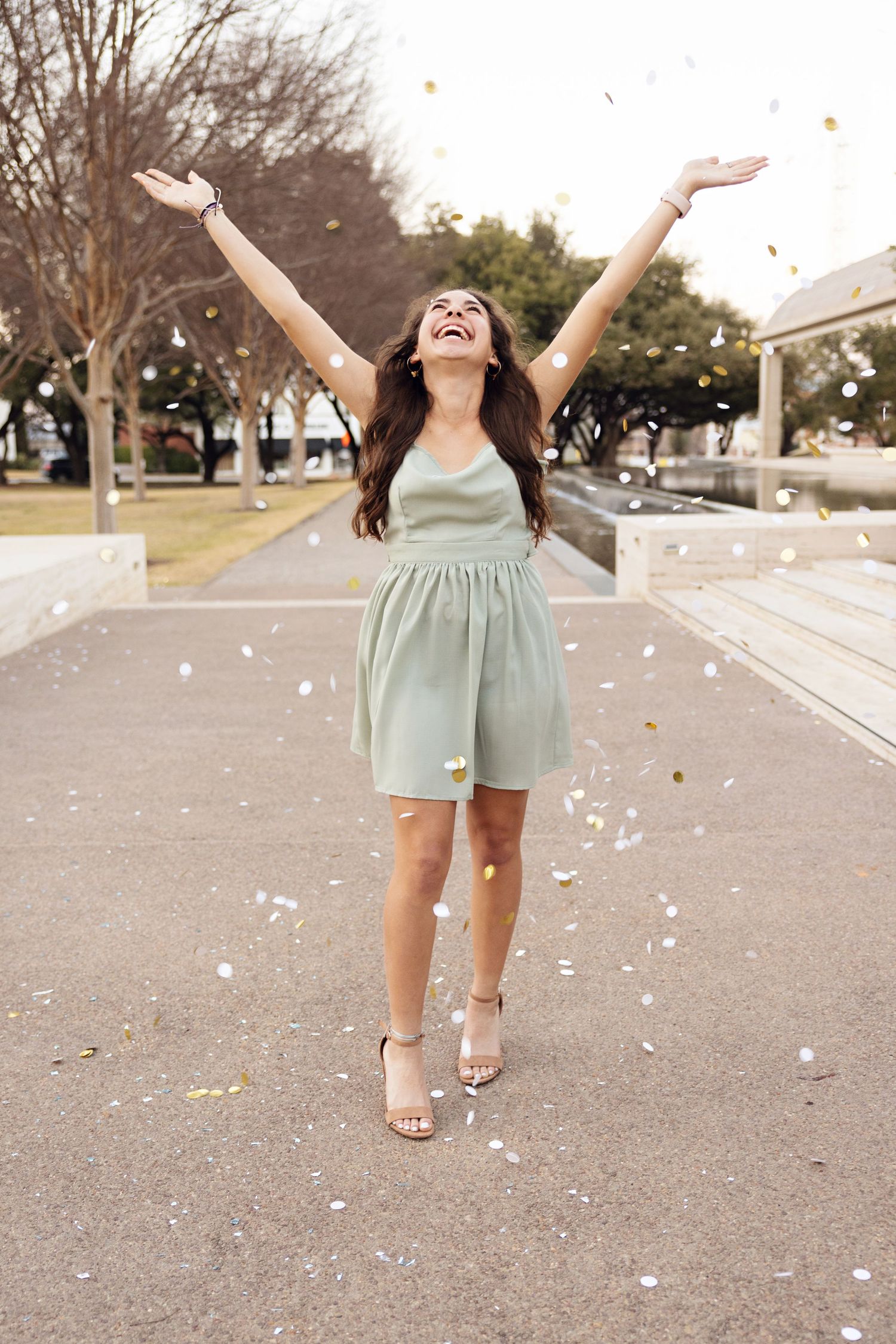 Young woman in mint dress celebrating with confetti flying around her outdoors.