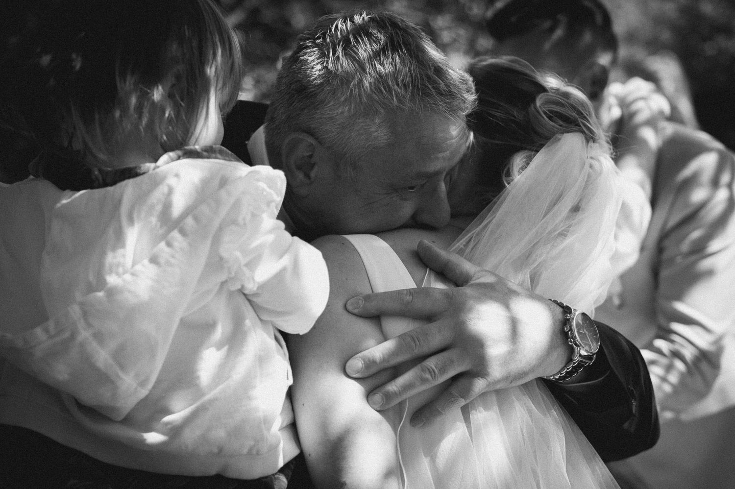 Black and white photo of a man in a suit embracing a bride in a wedding dress at a ceremony.