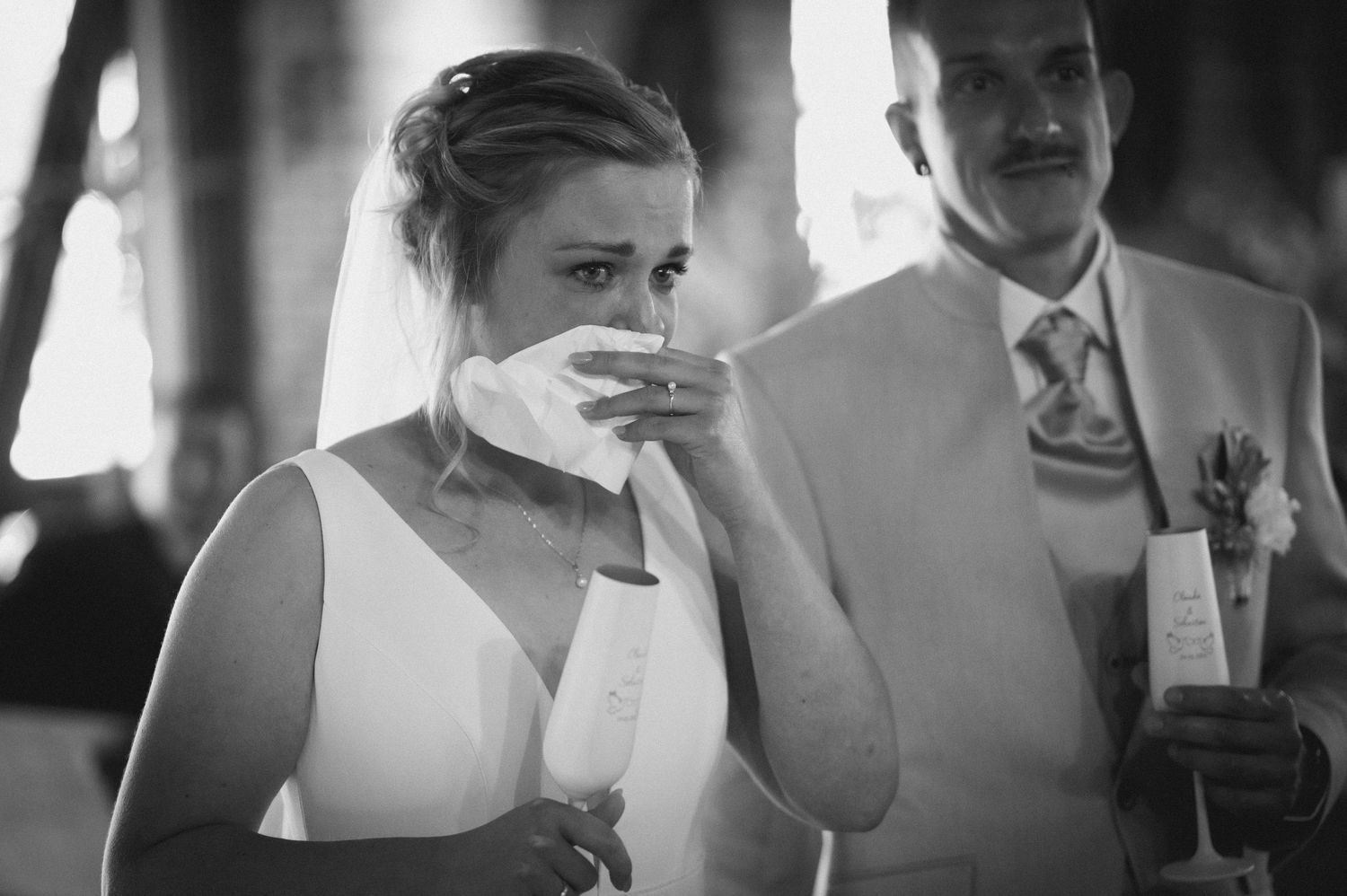 Black and white photo of an emotional bride wiping tears with a handkerchief during wedding ceremony.