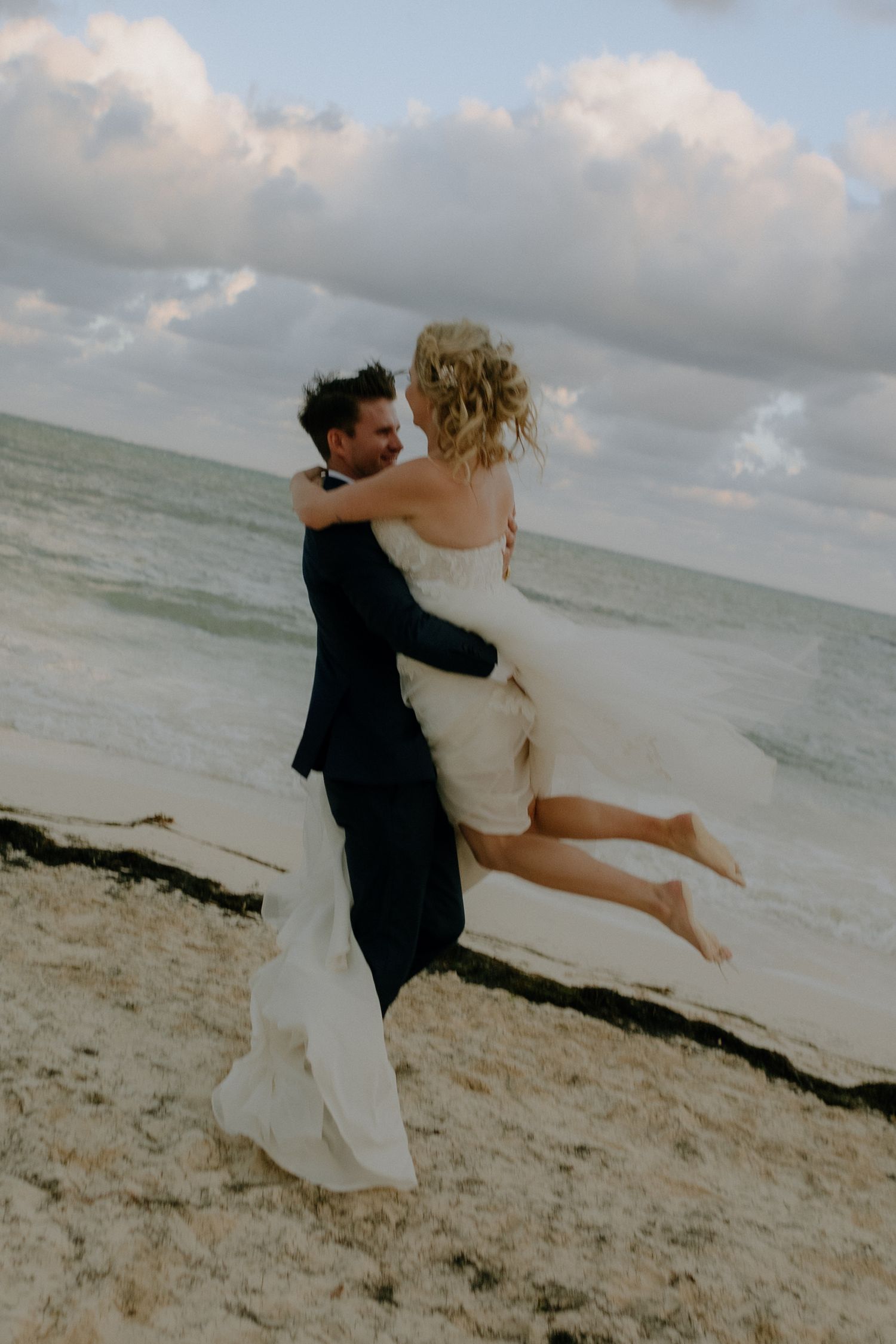 A joyful couple embraces on a beach as waves crash behind them while celebrating their wedding day.