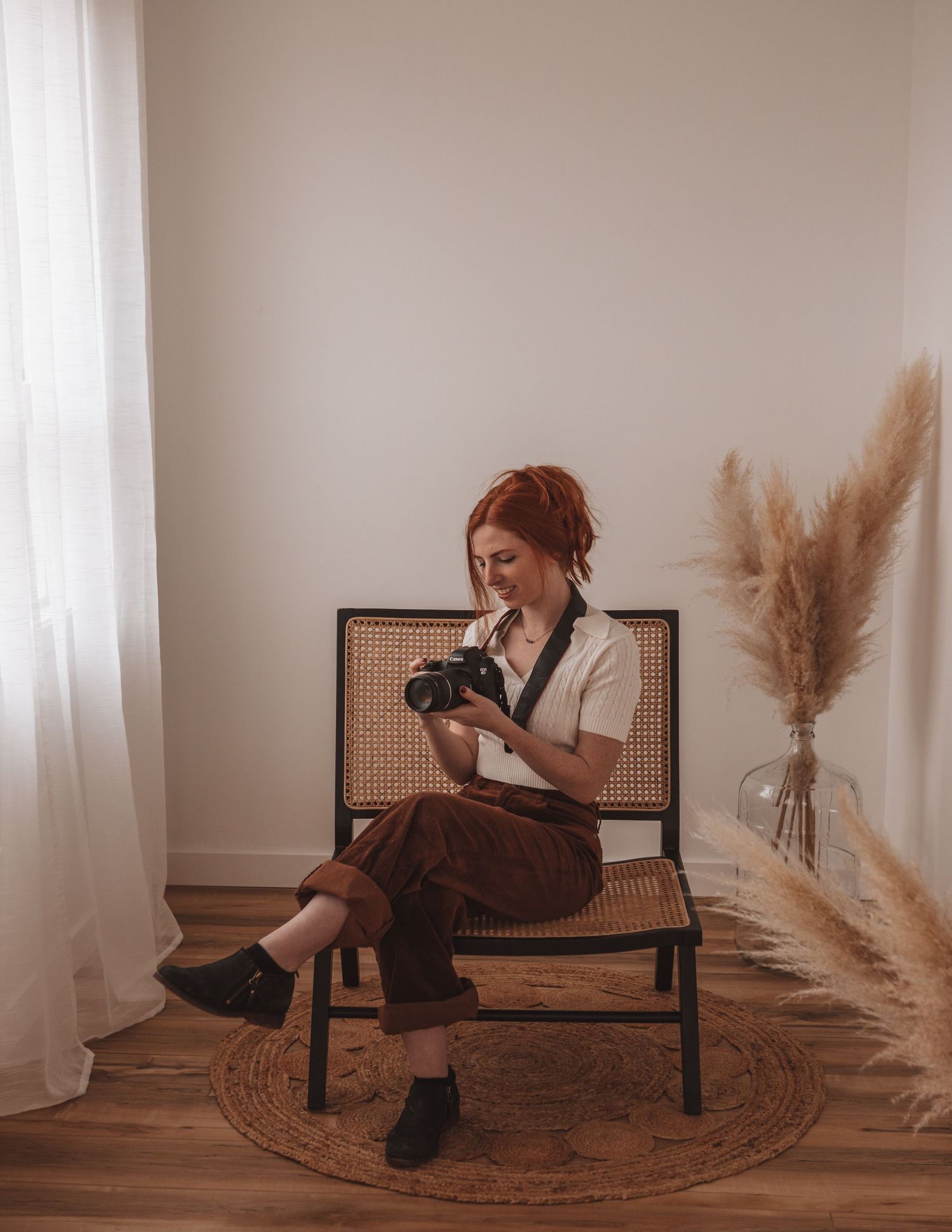 Person with red hair sits on a rattan chair reading, surrounded by pampas grass and natural decor.