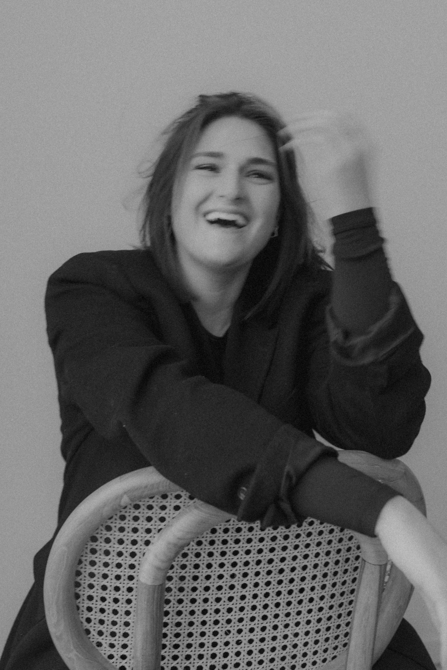 Black and white portrait of someone laughing joyfully while sitting on a woven chair.