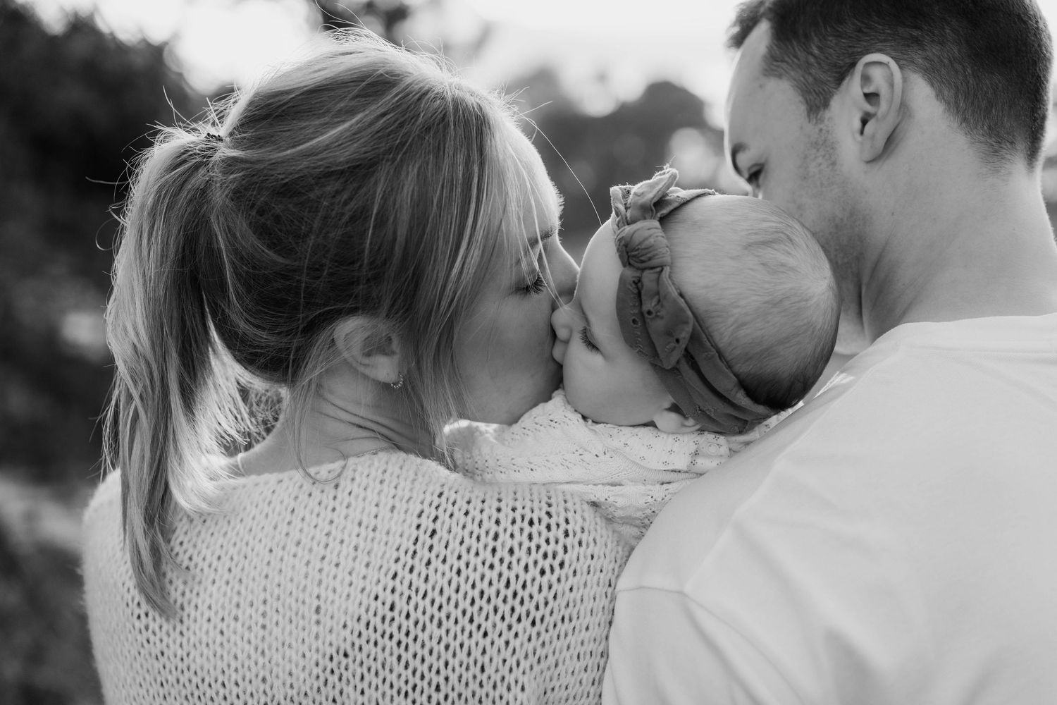 Black and white intimate family moment captured outdoors with soft natural lighting.