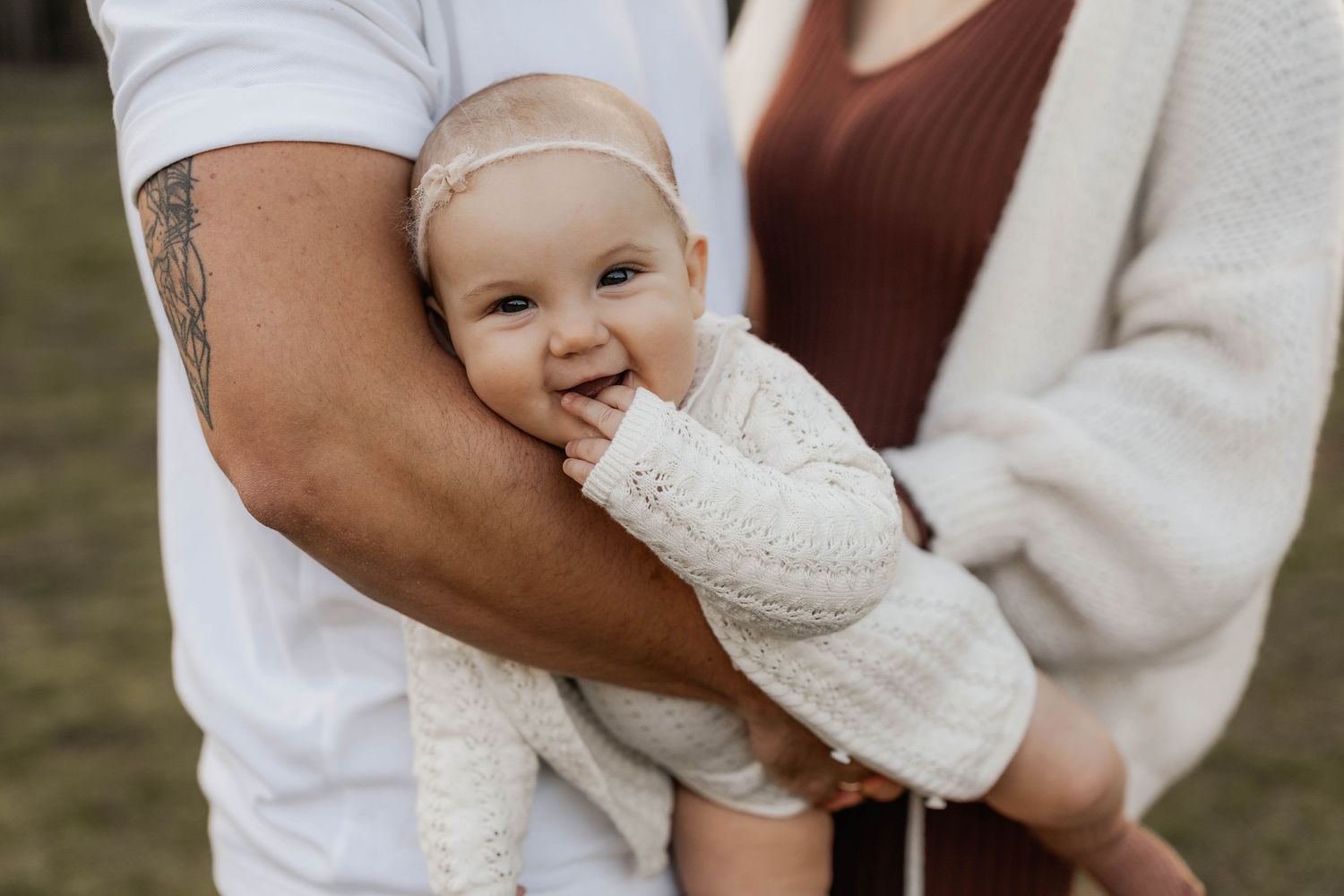 Close-up candid moment showing a baby in white knitwear against natural outdoor backdrop.