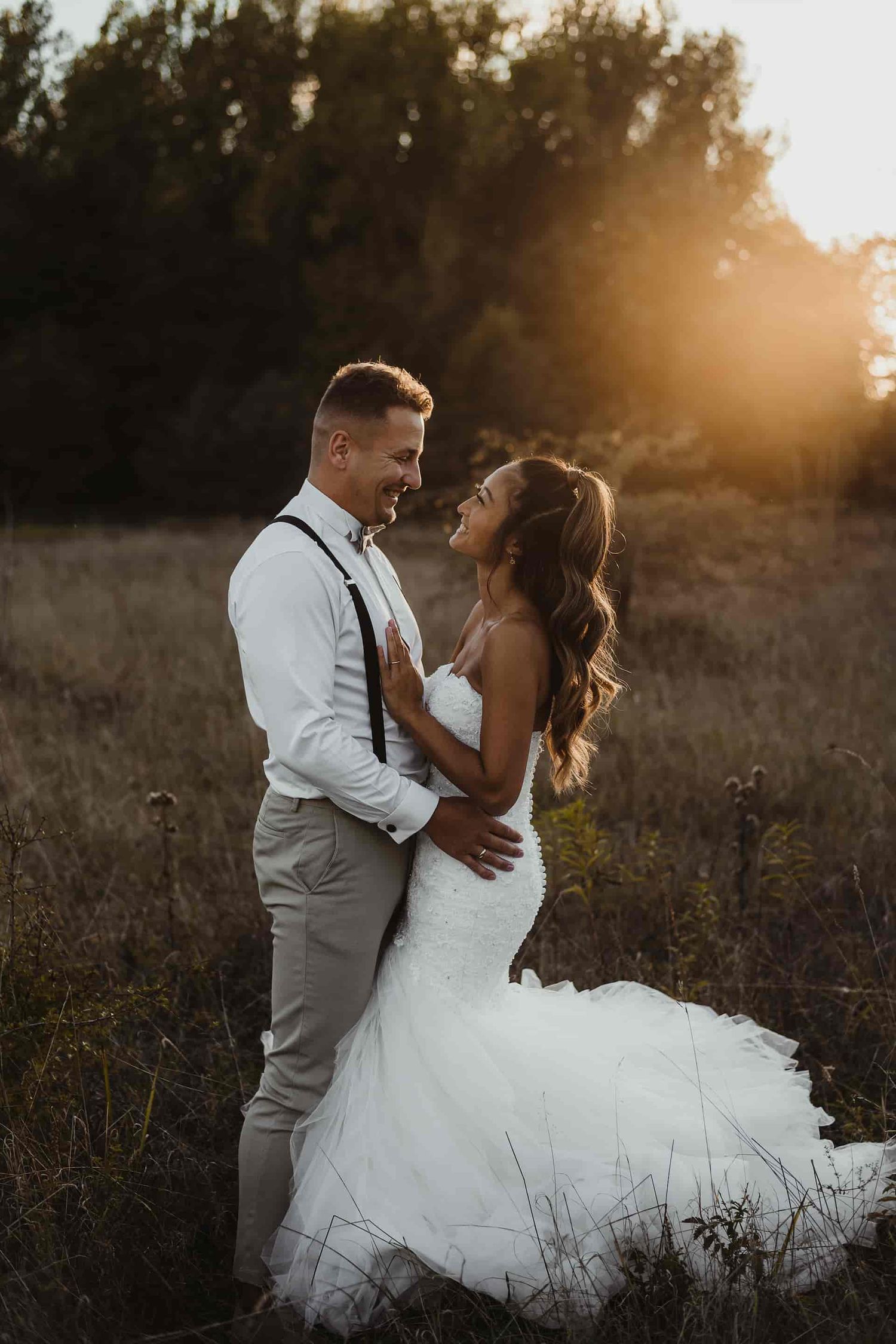 A romantic sunset wedding photoshoot captures a couple dancing in a golden meadow with soft backlit glow.