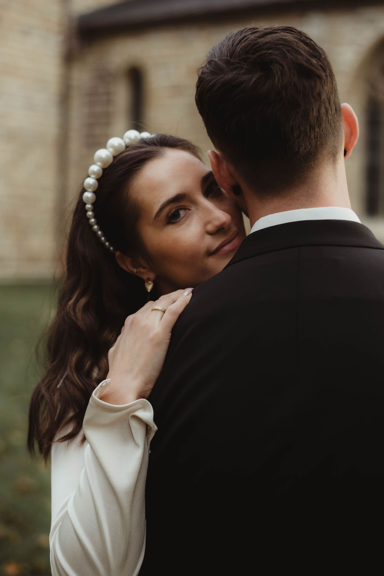 A tender wedding portrait showing a pearl-adorned bride with flowing dark hair embracing her groom.