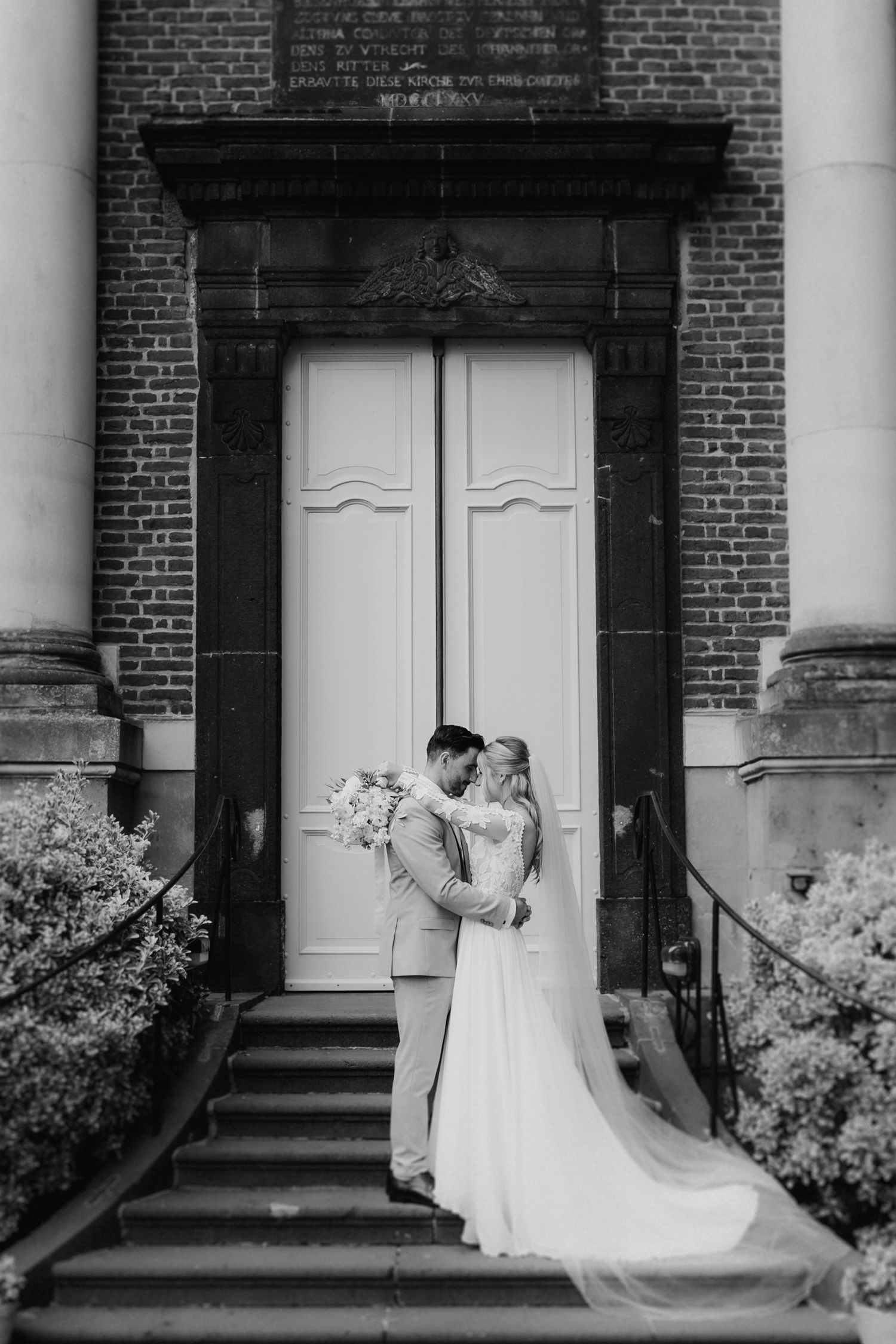 A black and white photo series showing a couple in wedding attire posing in front of a brick building with white doors.