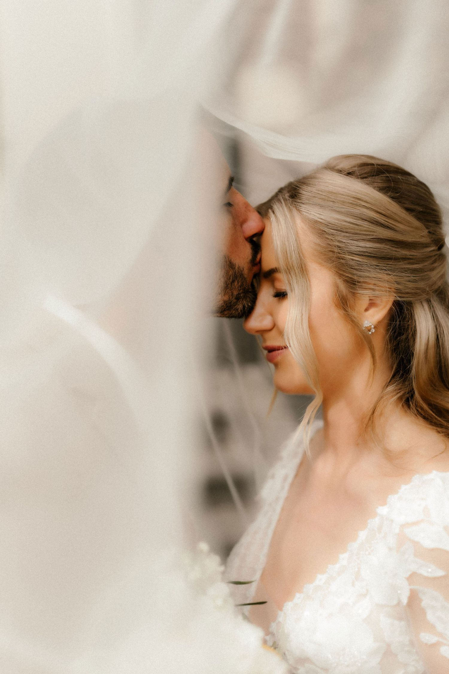 A bride in a white lace gown with an elegant updo hairstyle smiles during a wedding photo session.