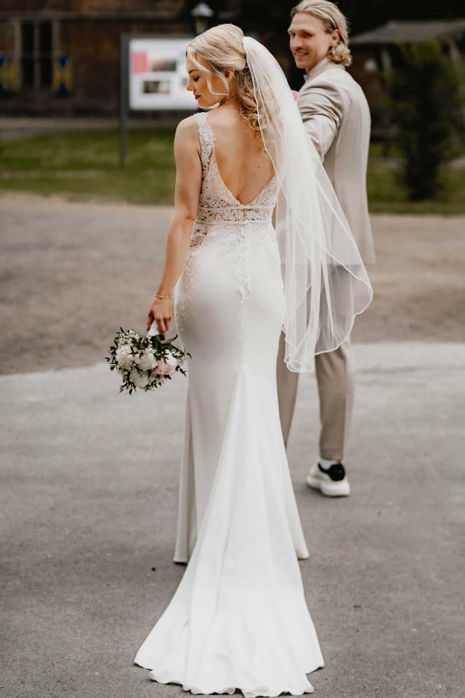 A bride in an elegant white wedding dress with a flowing veil holds a bouquet while walking outdoors.