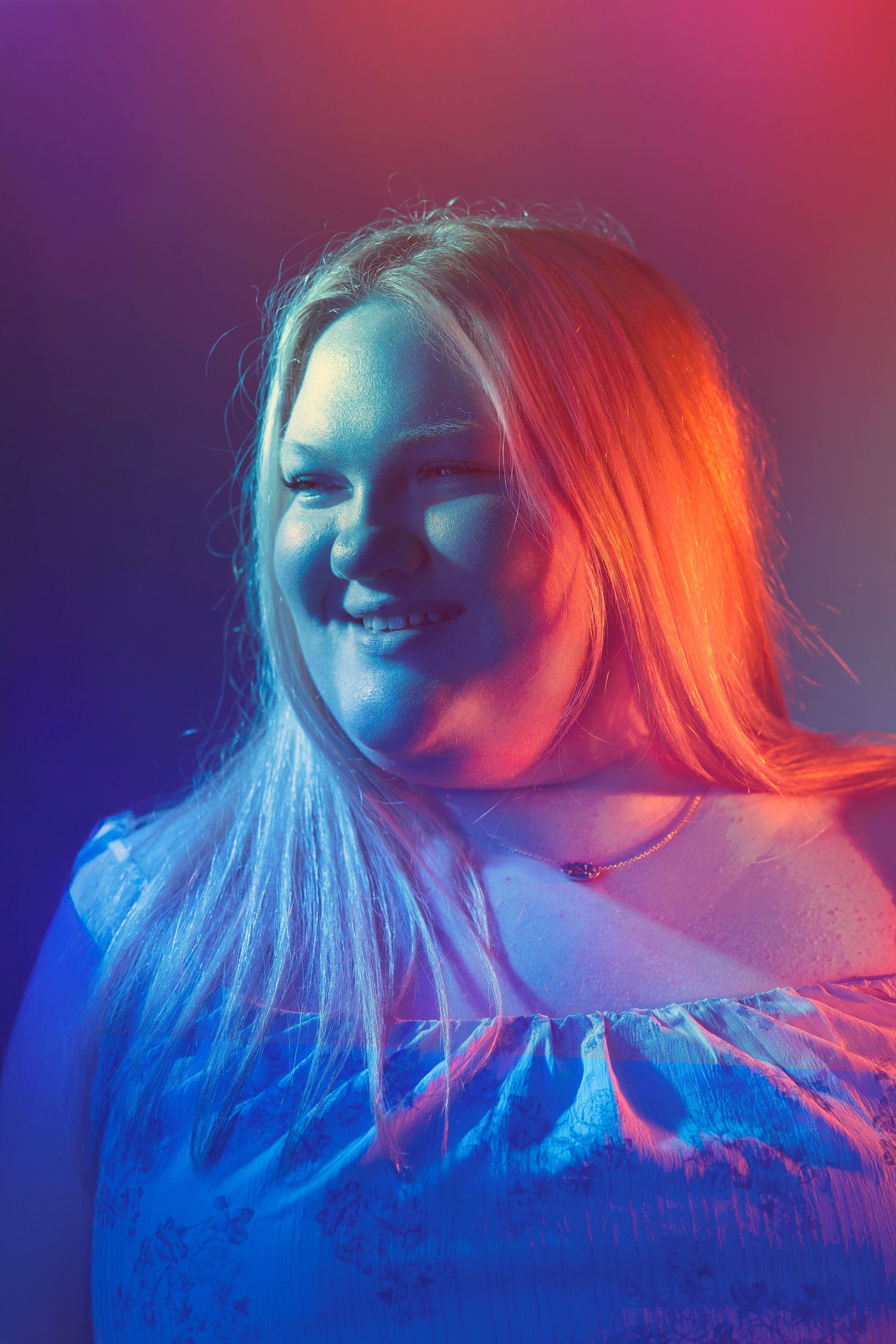 Smiling blonde woman portrait with vibrant blue and orange neon lighting effect.