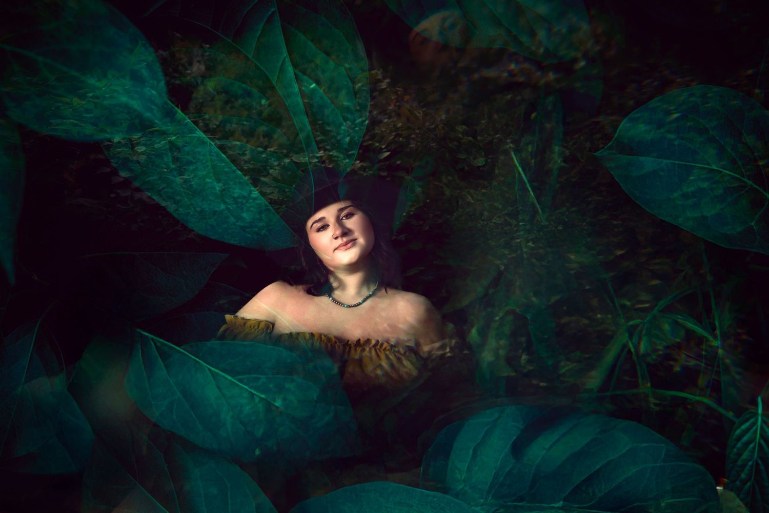 Smiling person surrounded by large tropical green leaves in dark forest setting.