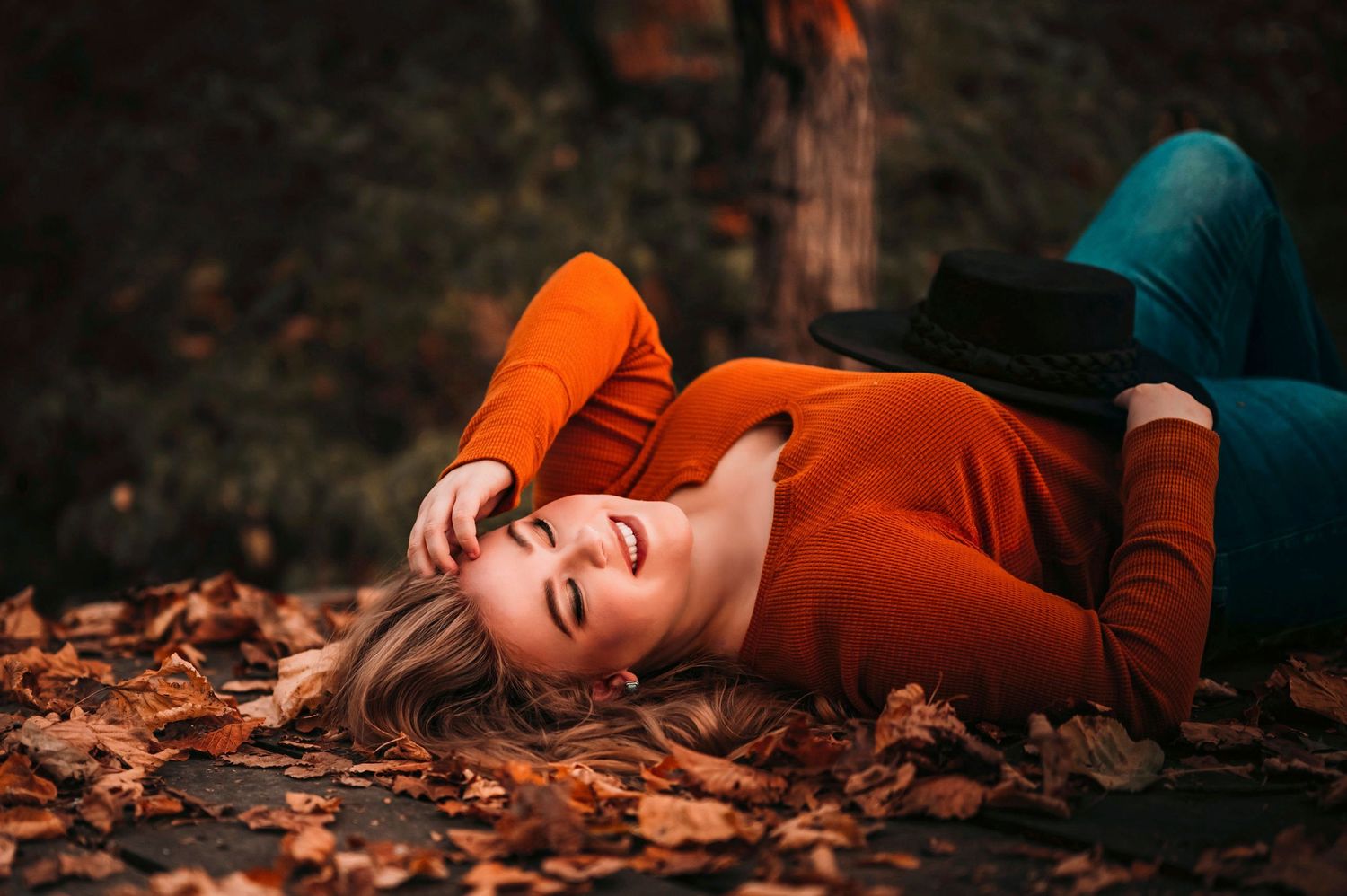 Smiling blonde woman in red sweater lying on autumn leaves in a park.
