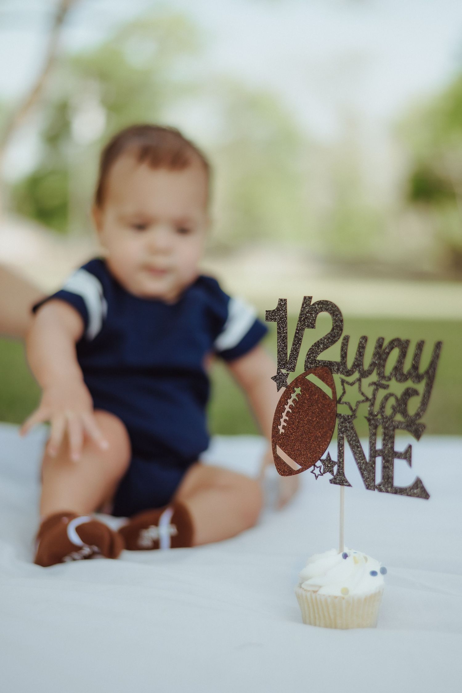A white cupcake with football-themed decorations and blue props sits on a table during a first birthday celebration.